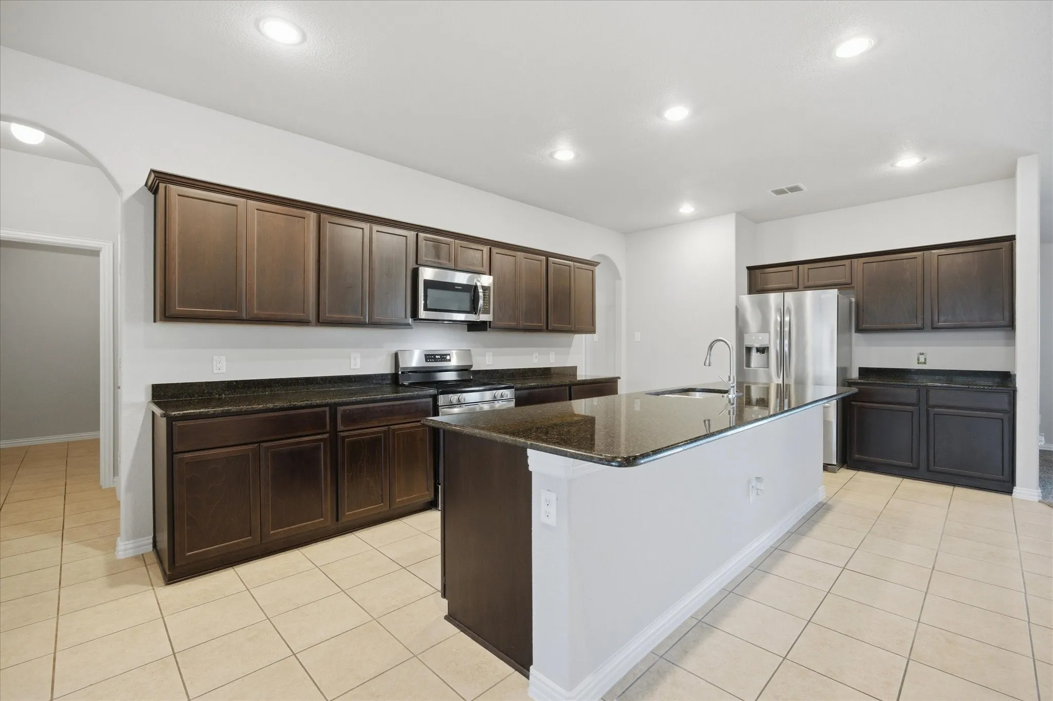 Kitchen featuring dark wood-finish cabinetry, stainless steel appliances, a center island with sink, and tile flooring