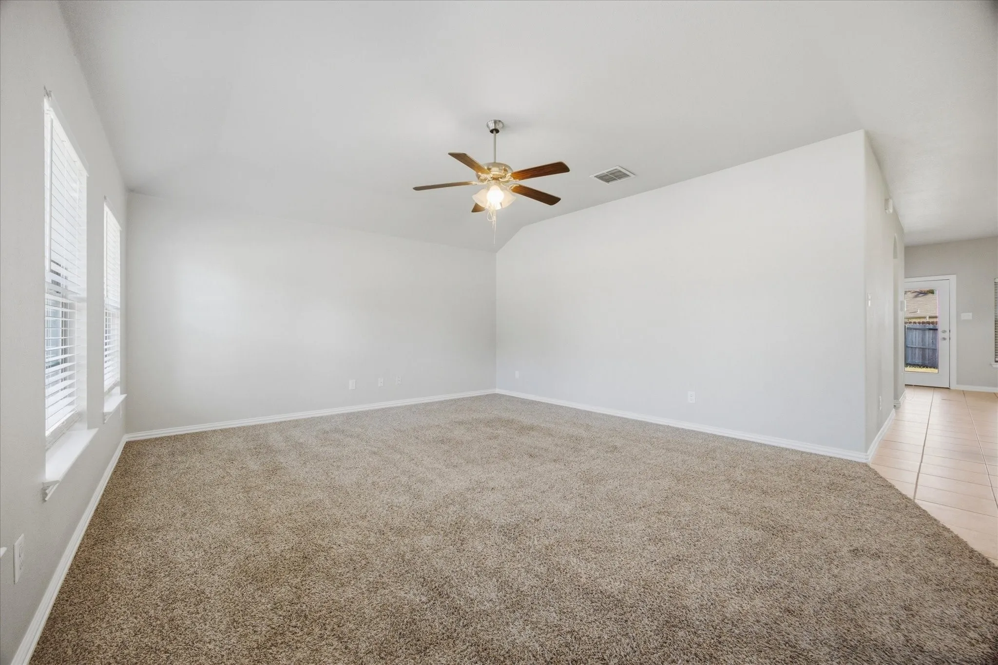 Spacious room with plush carpeting, neutral wall finishes, and multiple windows for natural light