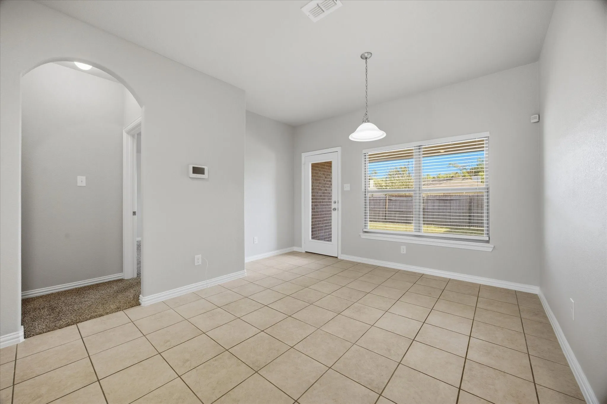 Neutral-toned tile flooring, pendant light fixture, arched doorway, and ample natural light from exterior windows
