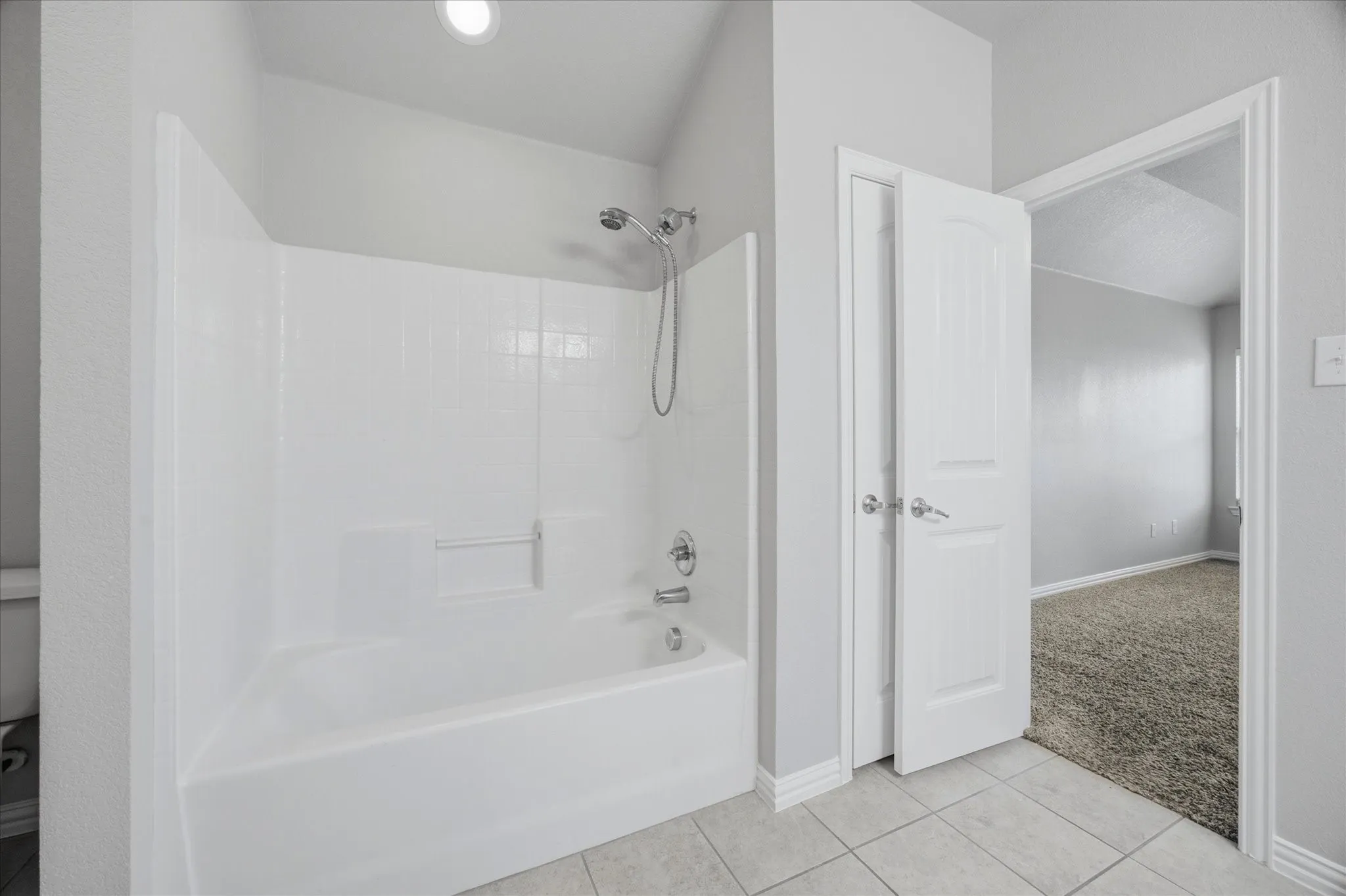 White tub and shower combination with a fixed showerhead and handheld sprayer, set against a light gray wall