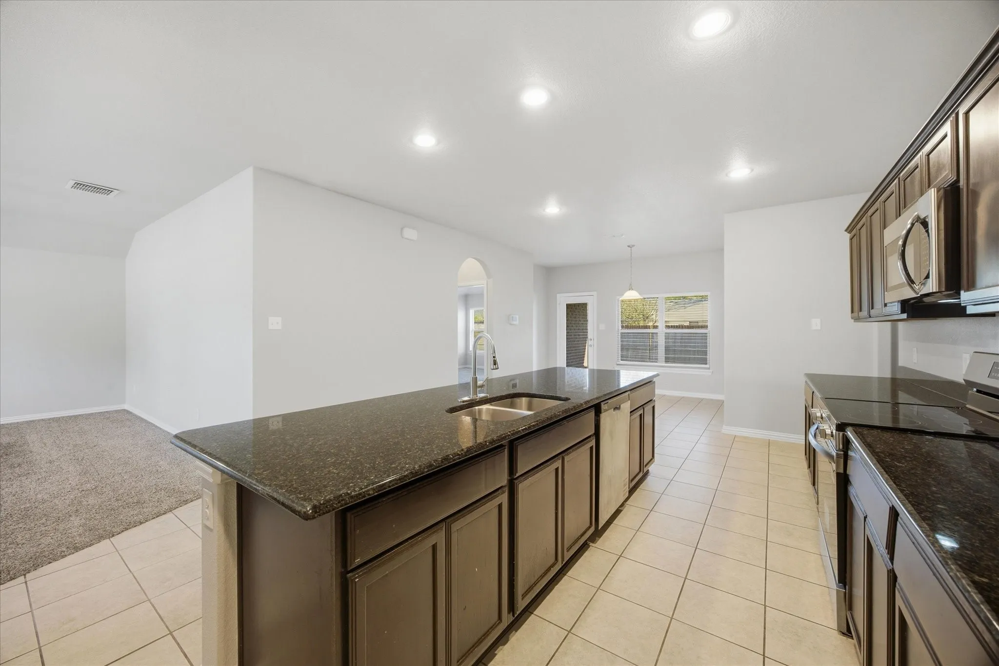 Kitchen featuring dark cabinetry, dark countertops, a stainless steel sink with a high-arc faucet, and integrated stainless steel appliances