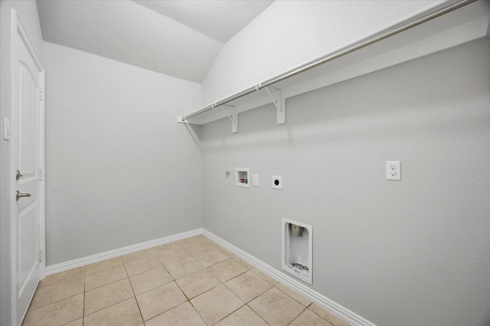 Vaulted ceiling laundry area with tile flooring and a built-in storage shelf and clothing rod