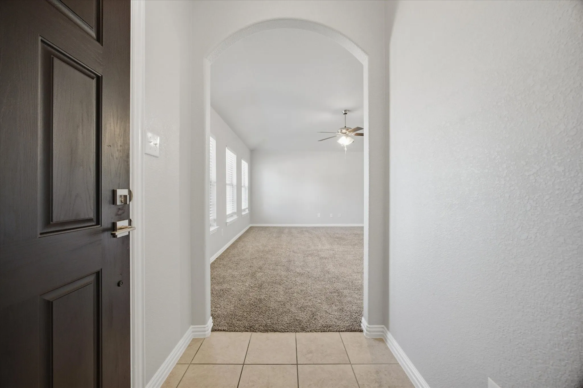 Bright hallway with arched entryway, ceramic tile flooring, and ceiling fan