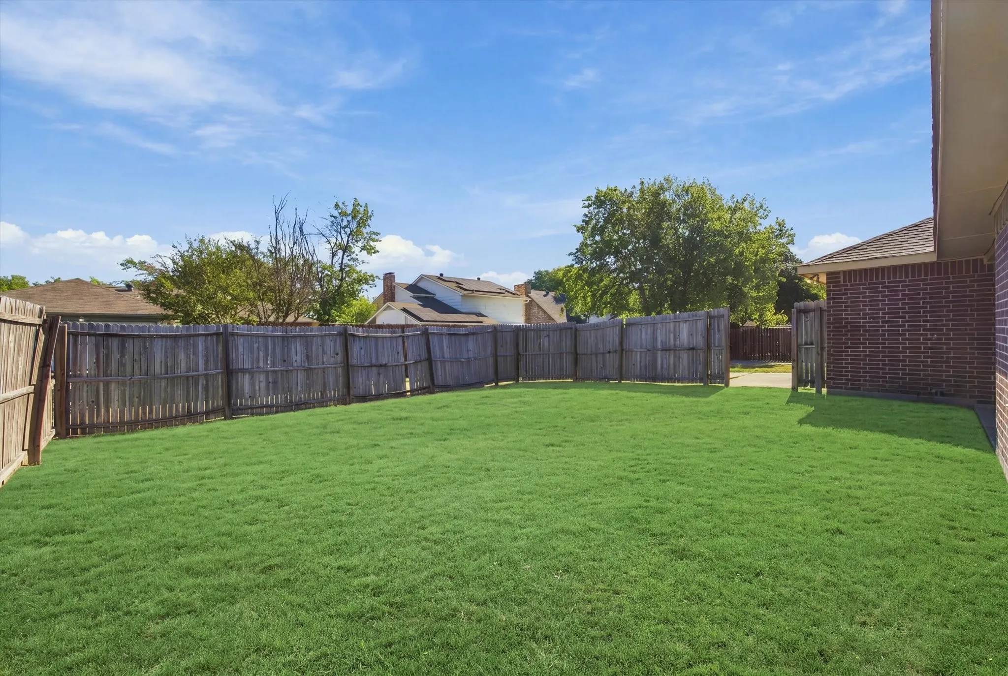 Expansive backyard featuring a meticulously manicured lawn, mature landscaping with established trees, and sturdy wood-finish fencing that provides privacy and definition