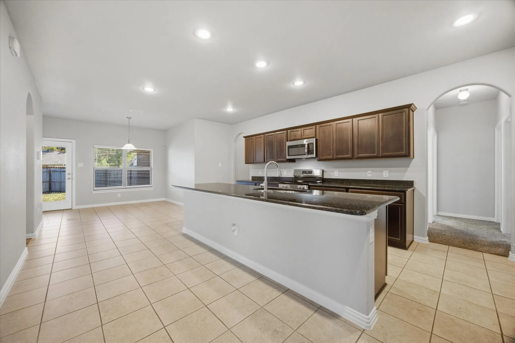Kitchen featuring dark wood-finish cabinetry, stainless steel appliances, a center island with a sink, and dark stone-finish countertops