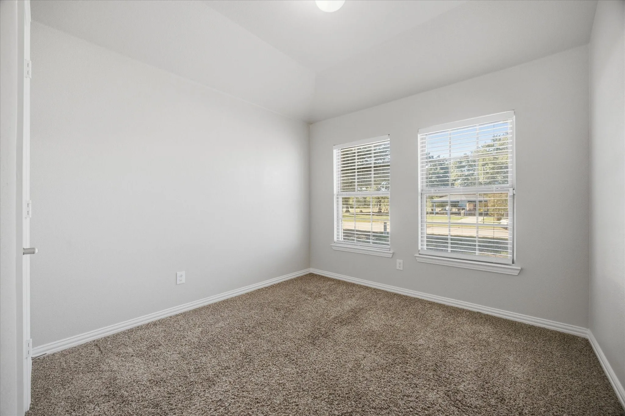 Vaulted ceiling, two windows with blinds, carpet flooring, and neutral wall paint