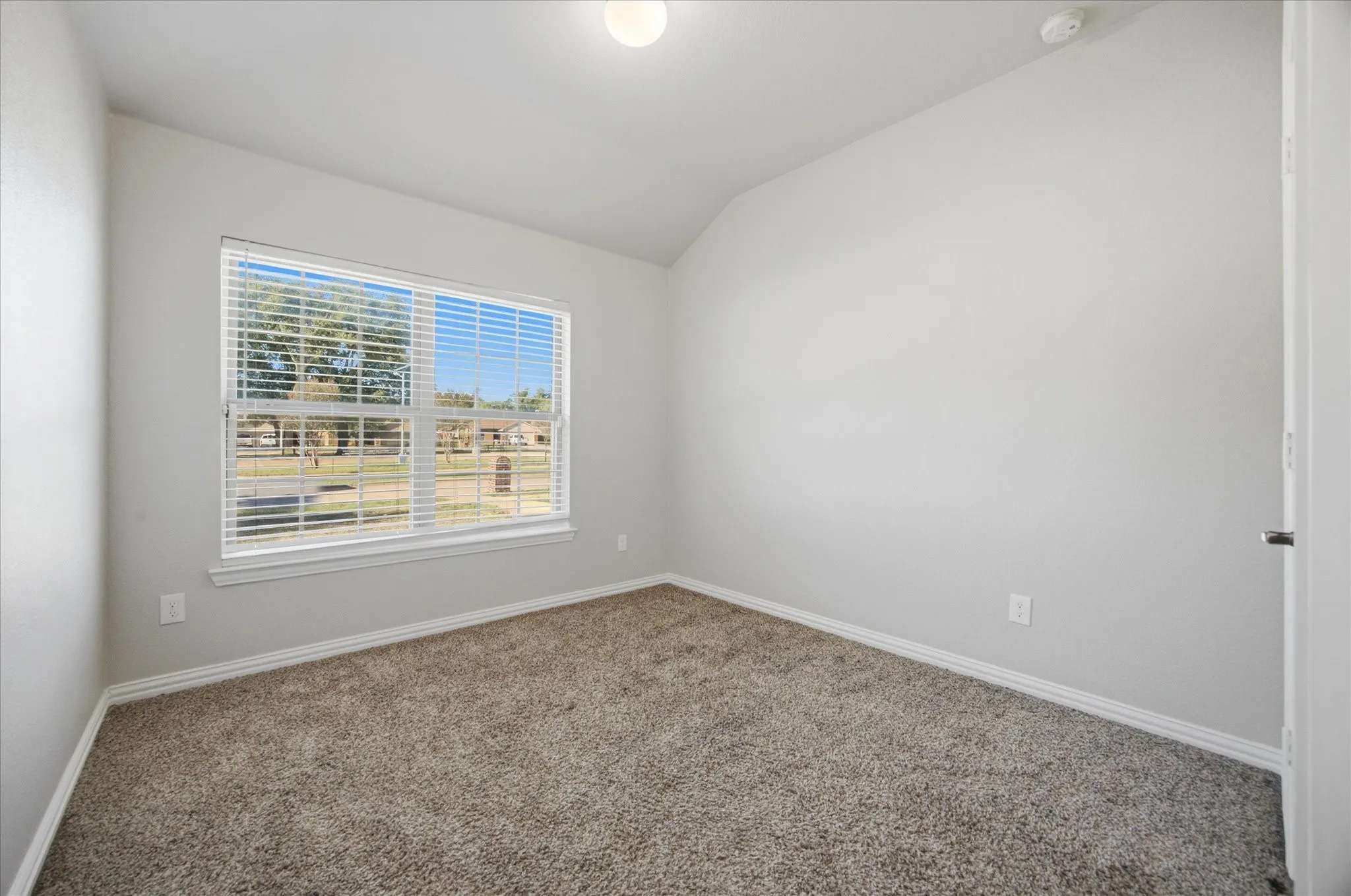 Neutral wall color, vaulted ceiling, recessed lighting, carpet flooring, and a large window with horizontal blinds