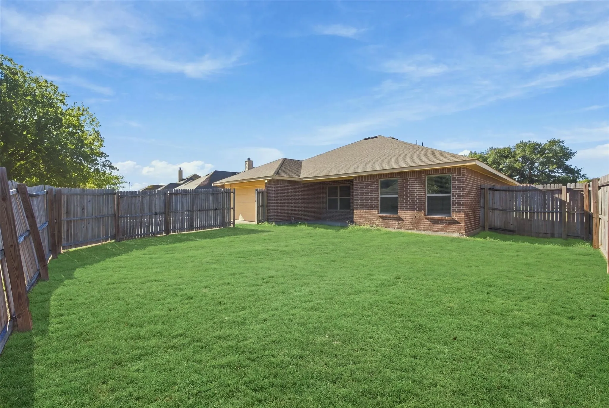 Expansive backyard featuring a brick exterior, shingle roof, and a wood fence