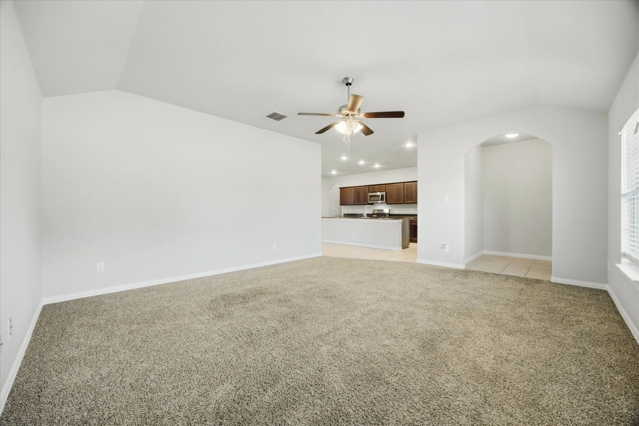 Vaulted ceiling with a ceiling fan, carpet flooring, arched doorway, recessed lighting, and kitchen with dark wood-finish cabinetry