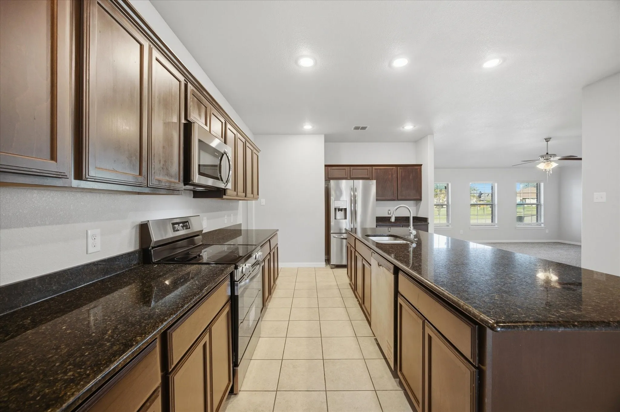 Galley kitchen featuring dark wood cabinetry, a large kitchen island, dark speckled countertops, stainless steel appliances, and tile flooring