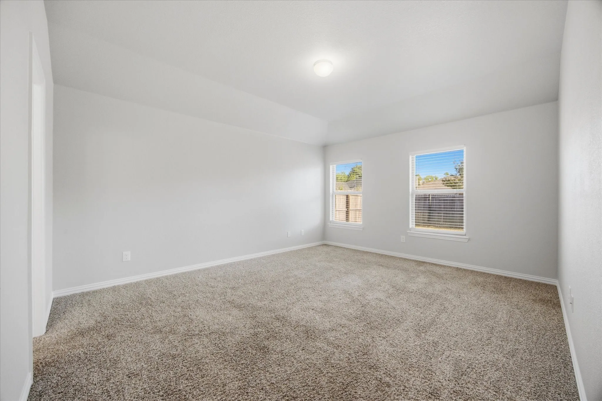 Neutral-toned carpeting, vaulted ceiling, and two windows with blinds
