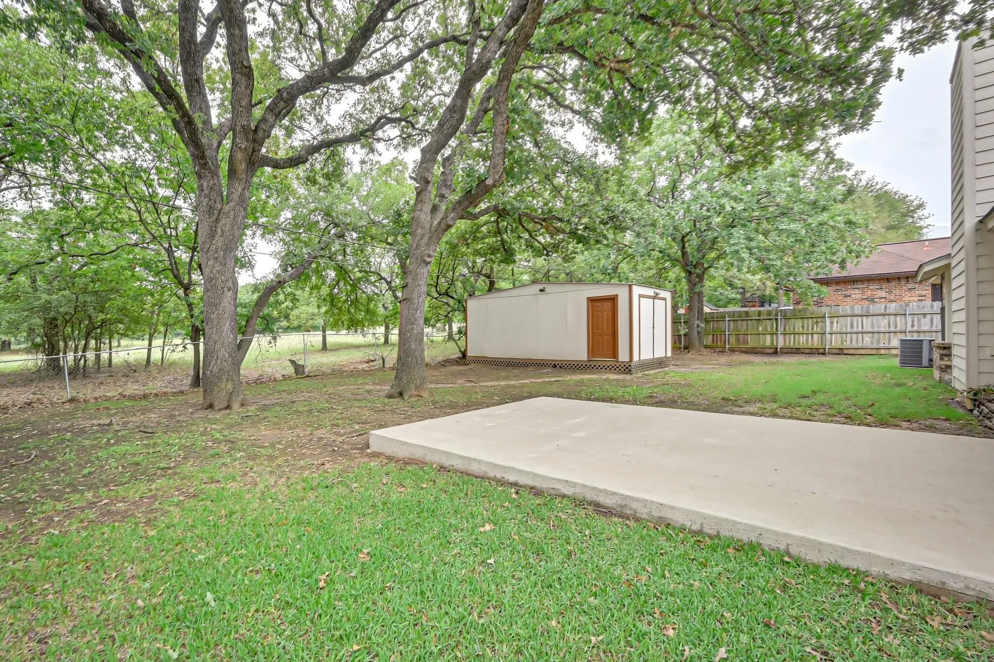 Expansive backyard featuring a concrete patio, a detached storage shed with a wood door, and mature trees