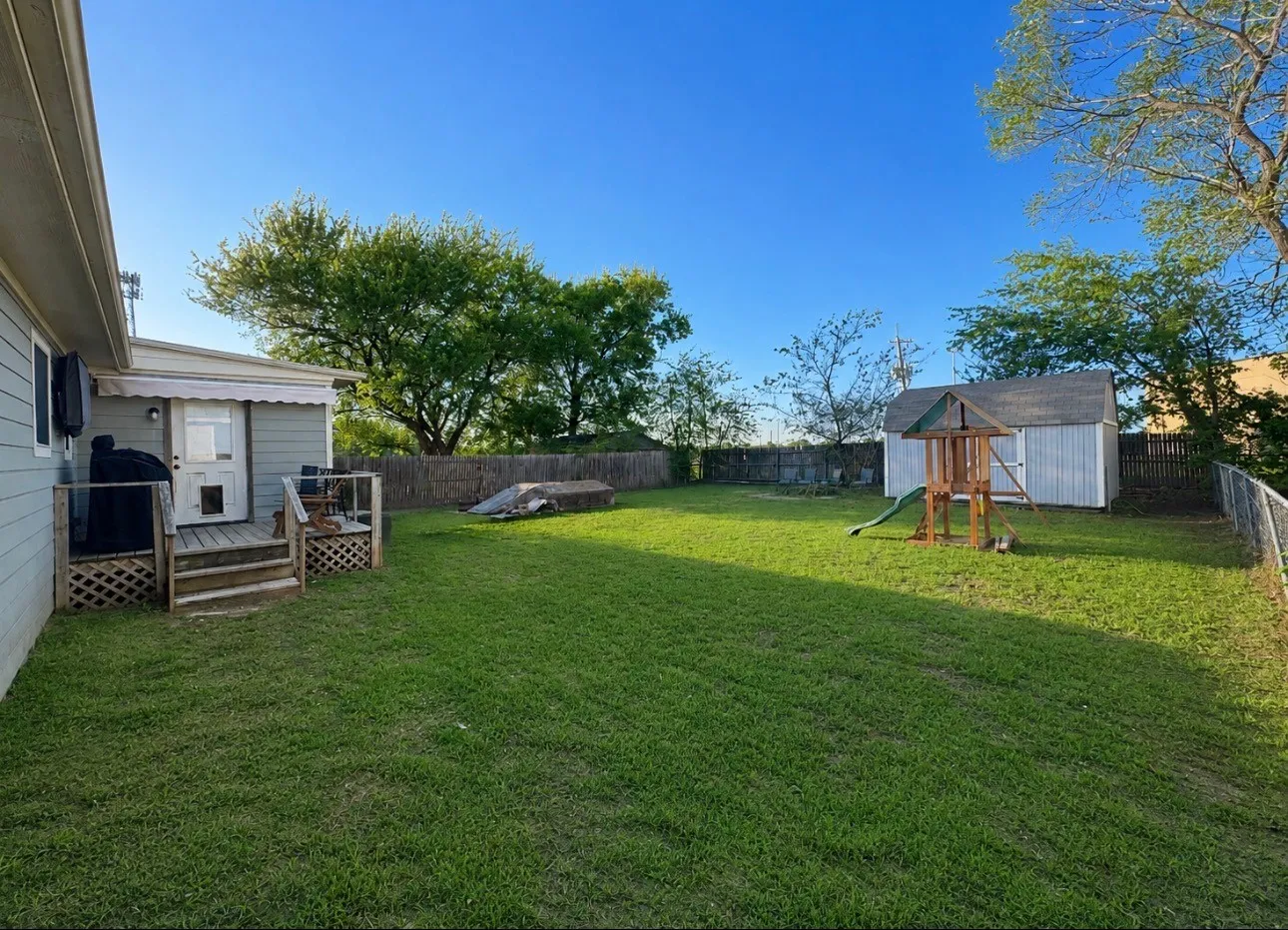 Expansive backyard featuring a manicured lawn, wood-constructed deck, and a white storage shed