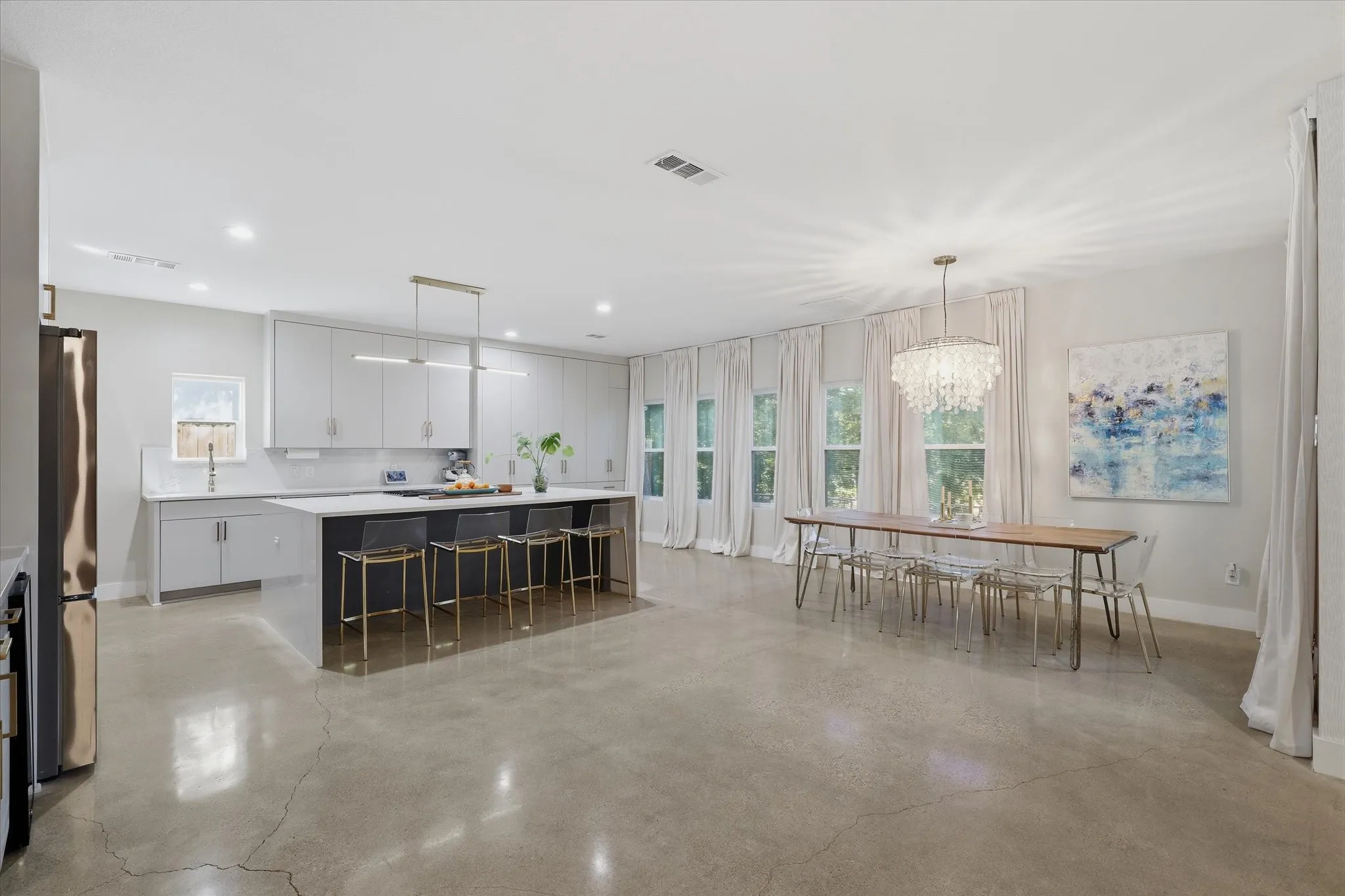 Polished concrete flooring, recessed lighting, white cabinetry, kitchen island with seating, and multiple windows