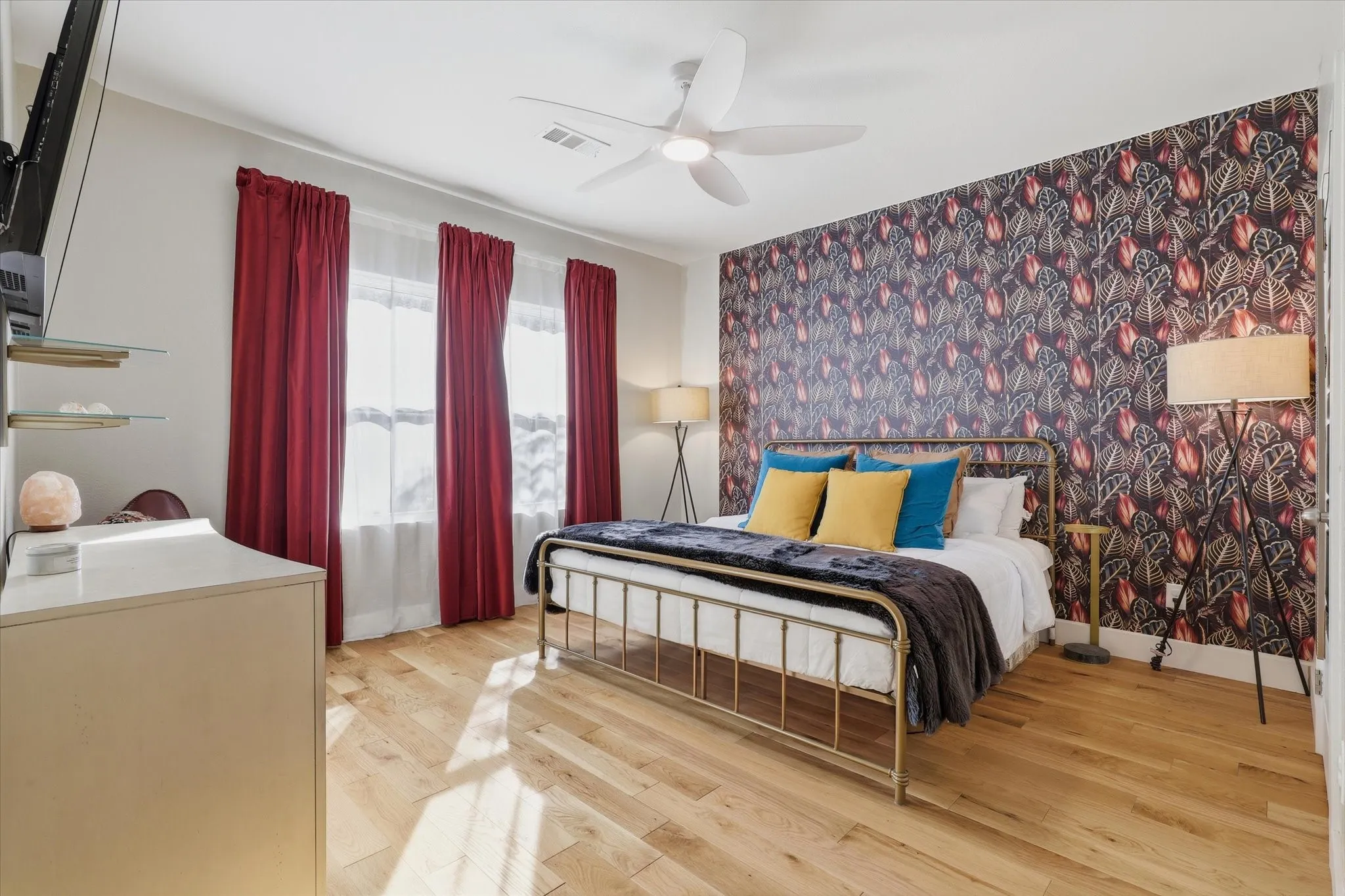 Light wood flooring, accent wall with patterned wallpaper, ceiling fan, and multiple windows