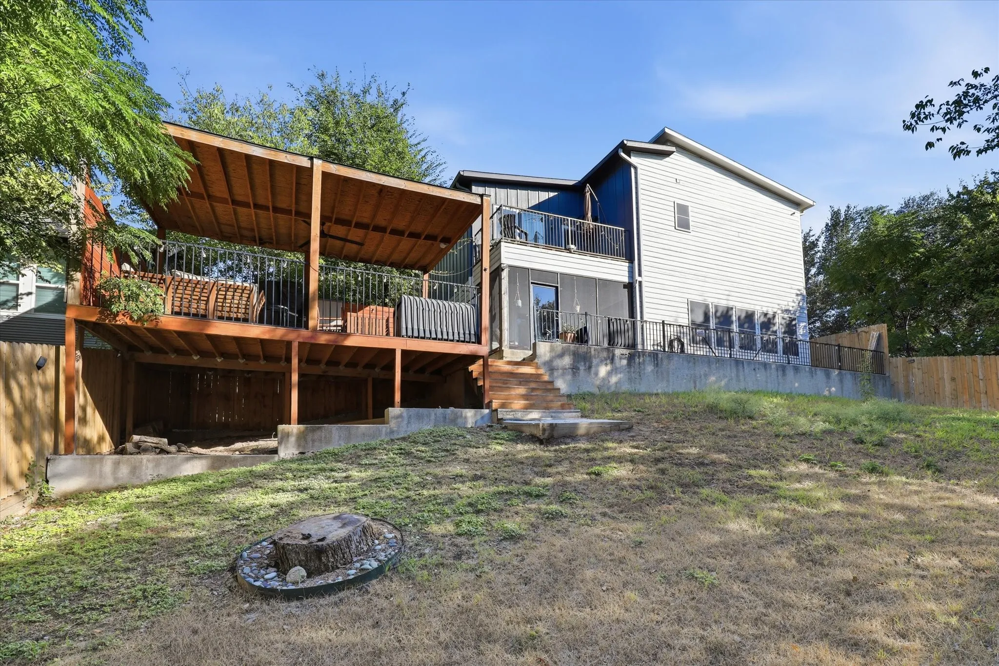 Multi-level wood deck with a partial covering, second-story balcony with metal railings, wood privacy fence, and concrete retaining walls