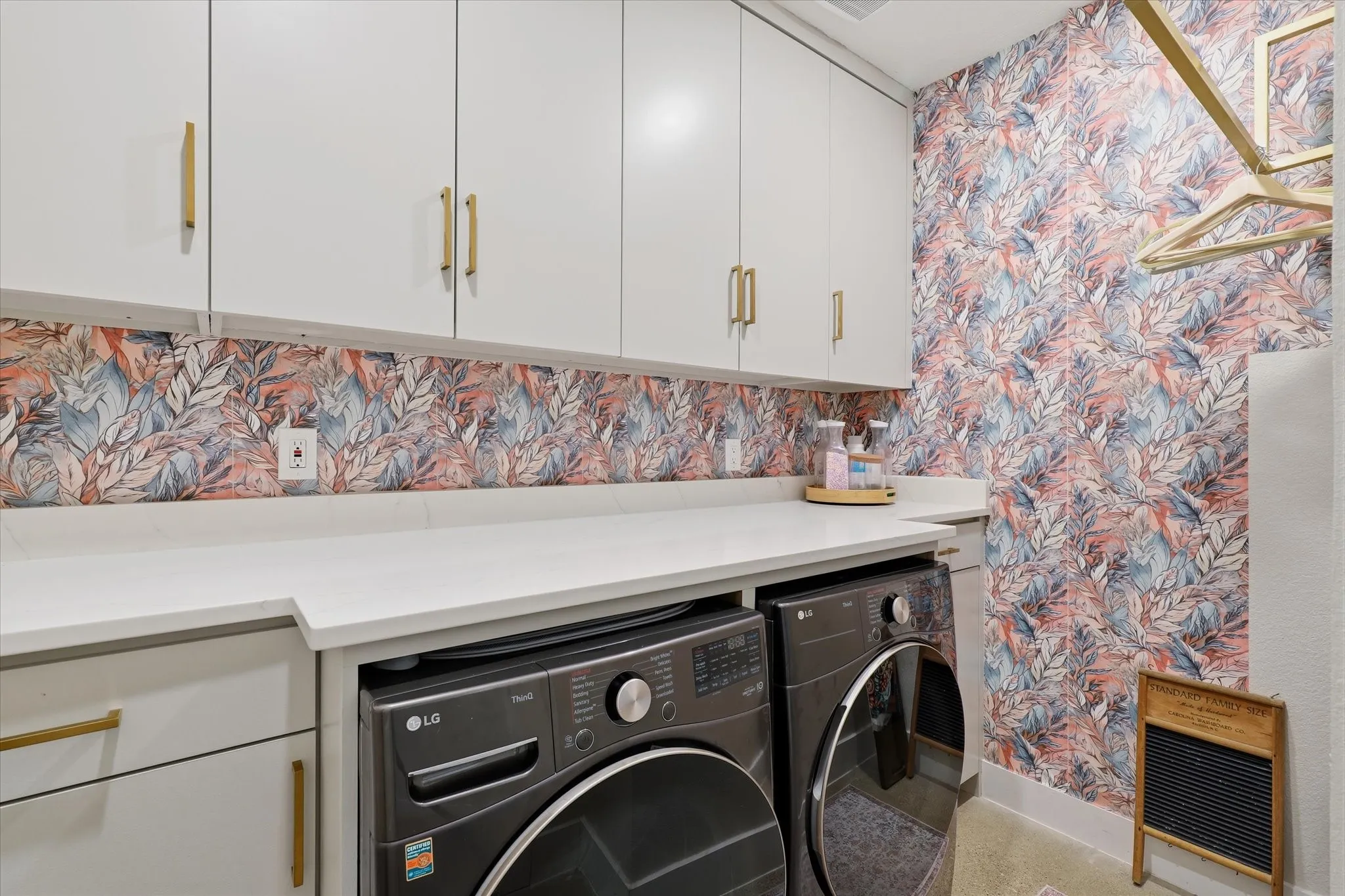 White cabinetry with gold-tone hardware, white countertops, and wallpaper