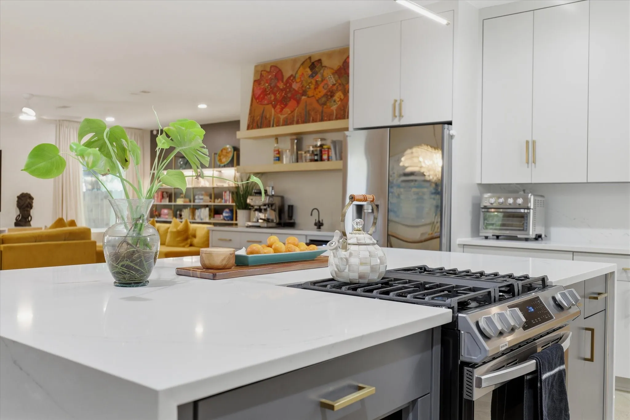 Kitchen island with integrated gas range, light countertops, white upper cabinetry, gray lower cabinetry, and stainless steel appliances