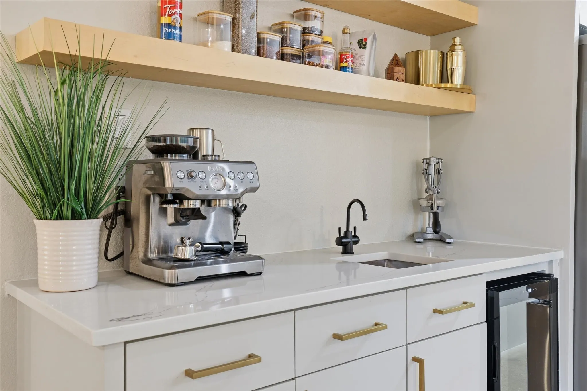 White countertop with an undermount sink, a matte black faucet, and light wood-finish floating shelves