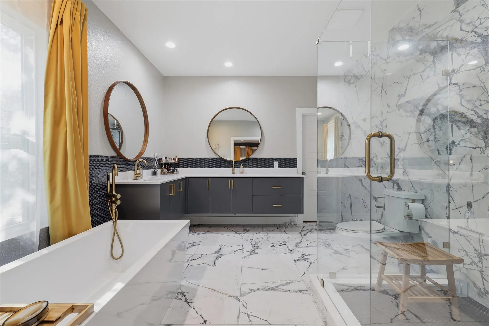 Dual vanity with integrated sinks, freestanding soaking tub, glass-enclosed shower, gold-finish fixtures, and marble-look flooring