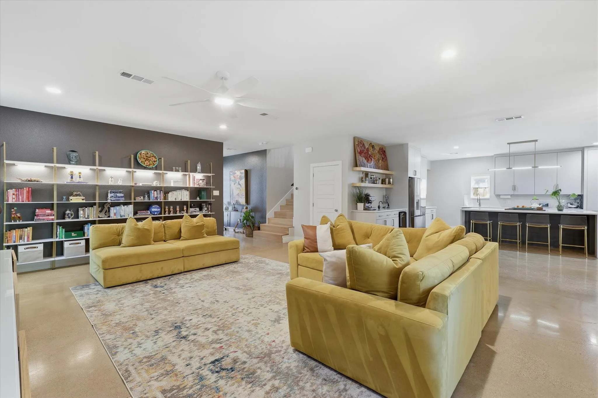 Open-concept living area featuring a built-in shelving system with integrated lighting, polished concrete flooring, recessed lighting, and a ceiling fan