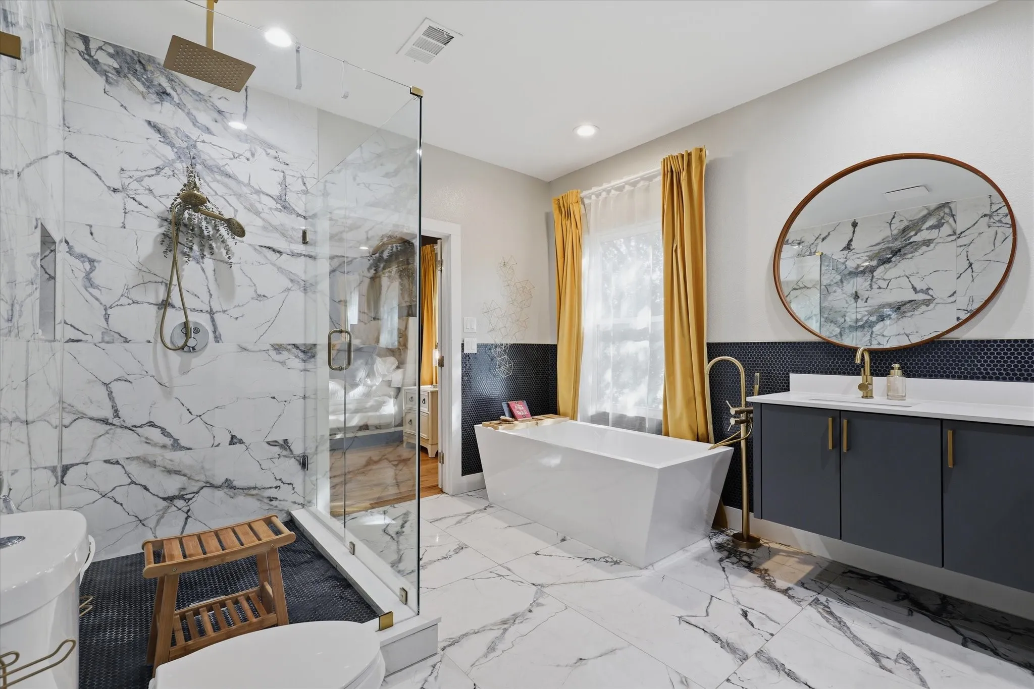 Walk-in shower with clear glass enclosure and rainfall showerhead, freestanding soaking tub with floor-mounted faucet, dual-sink vanity with quartz countertop, and large round mirror