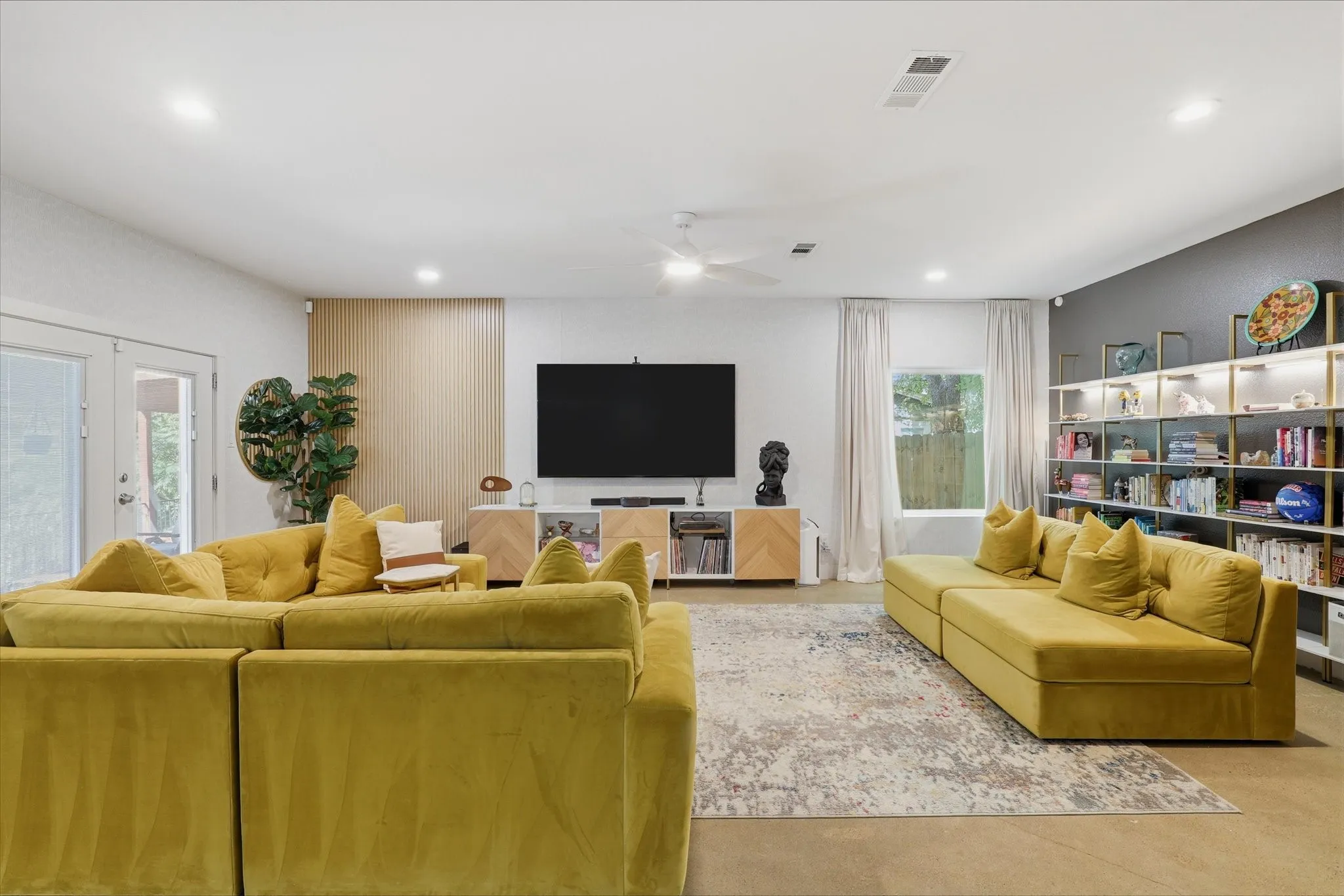 Vaulted ceiling with recessed lighting, exposed concrete flooring, built-in shelving, white double-pane glass doors, and a ceiling fan