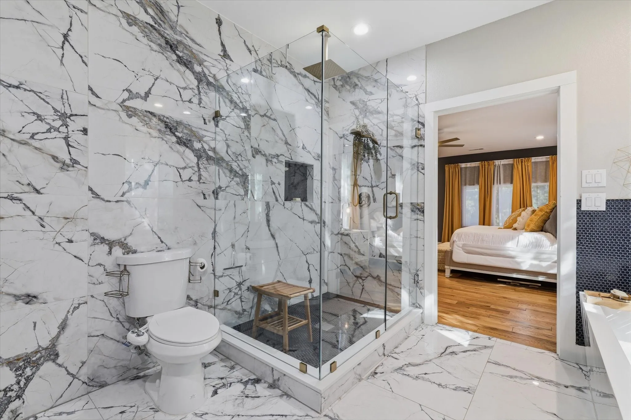 Glass-enclosed shower with a built-in niche, white and gray veined tile flooring, coordinating wall tile, and recessed lighting