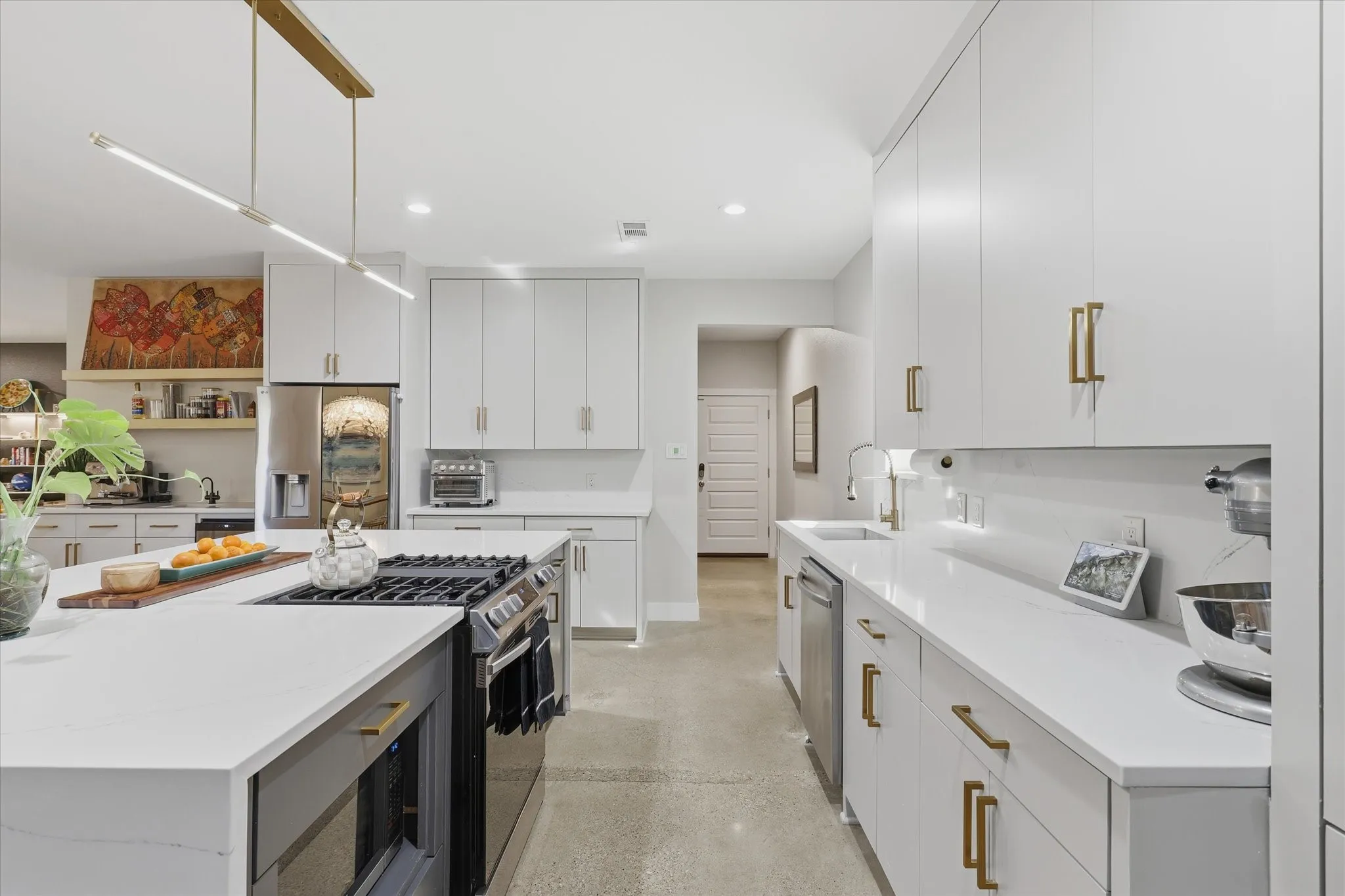 Kitchen featuring a central island with a gas range, white cabinetry with gold-tone hardware, a stainless steel refrigerator, and a linear pendant light fixture