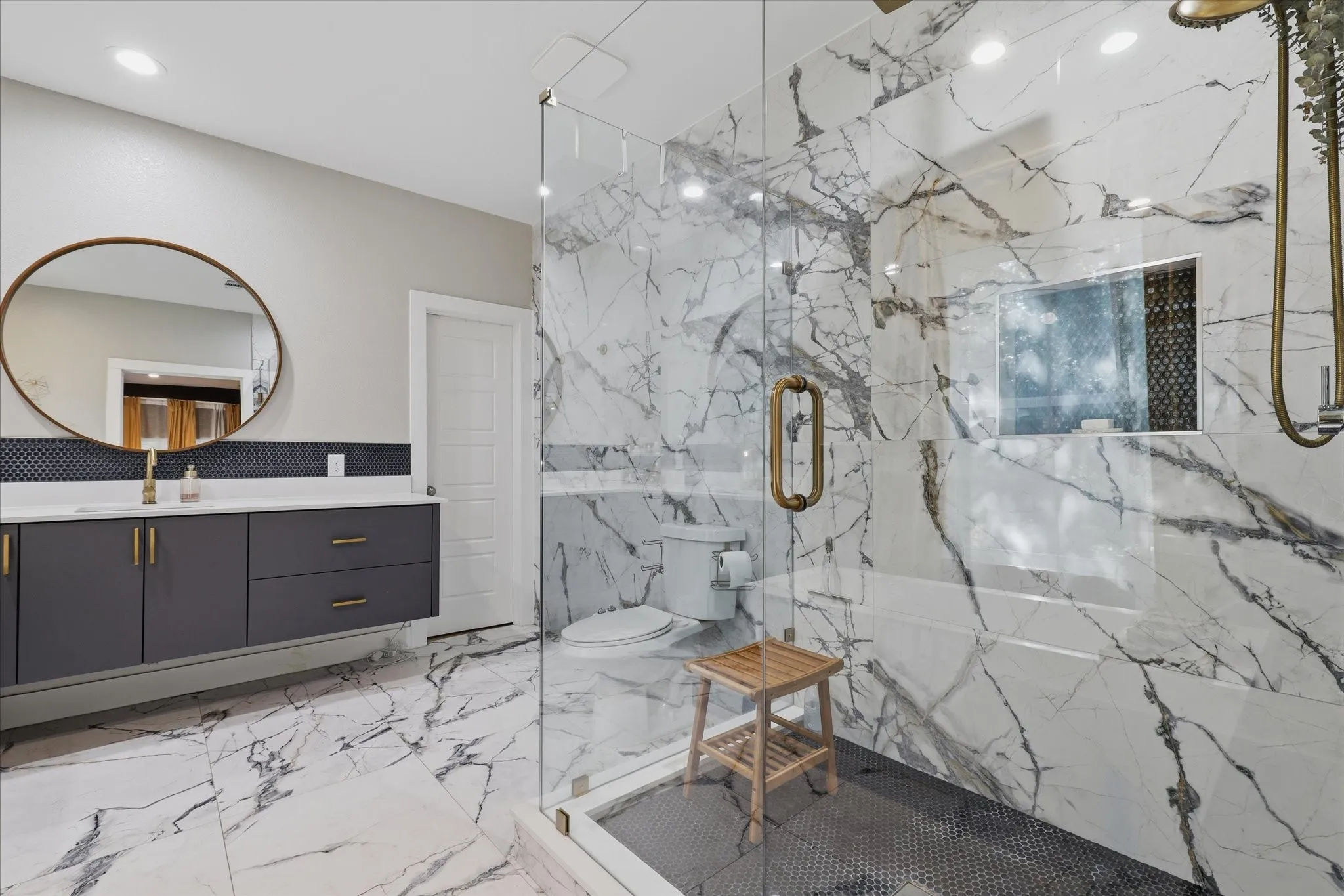 Spacious bathroom featuring a floating vanity with dark cabinetry, a frameless glass shower enclosure, and large format marble-look tile flooring