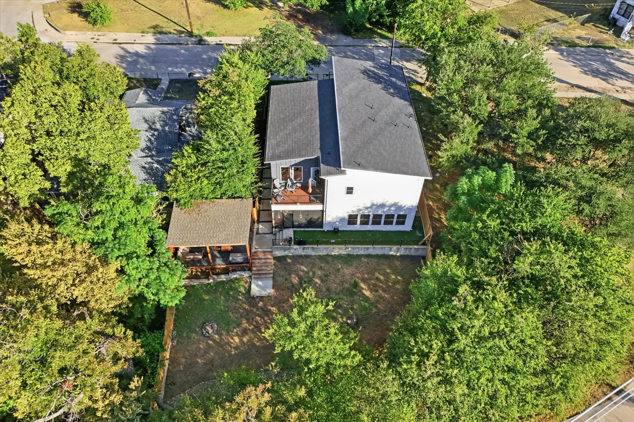 Contemporary residential structure featuring a gray shingle roof, a second-story balcony with railings, a covered outdoor structure, and a fenced yard