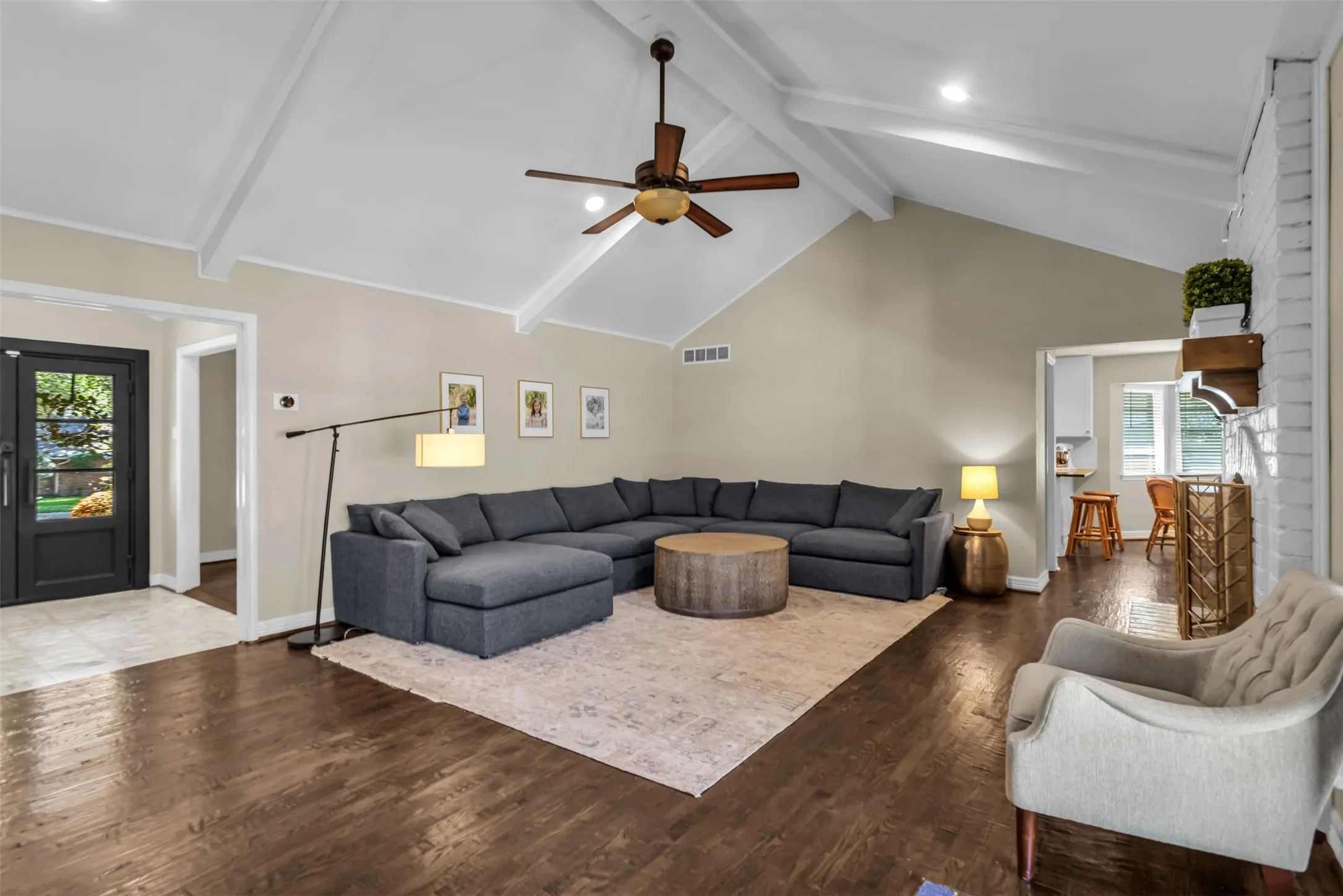 Spacious great room showcasing soaring vaulted ceilings with exposed white beams, wood-finish flooring throughout, and a ceiling fan with bronze finish