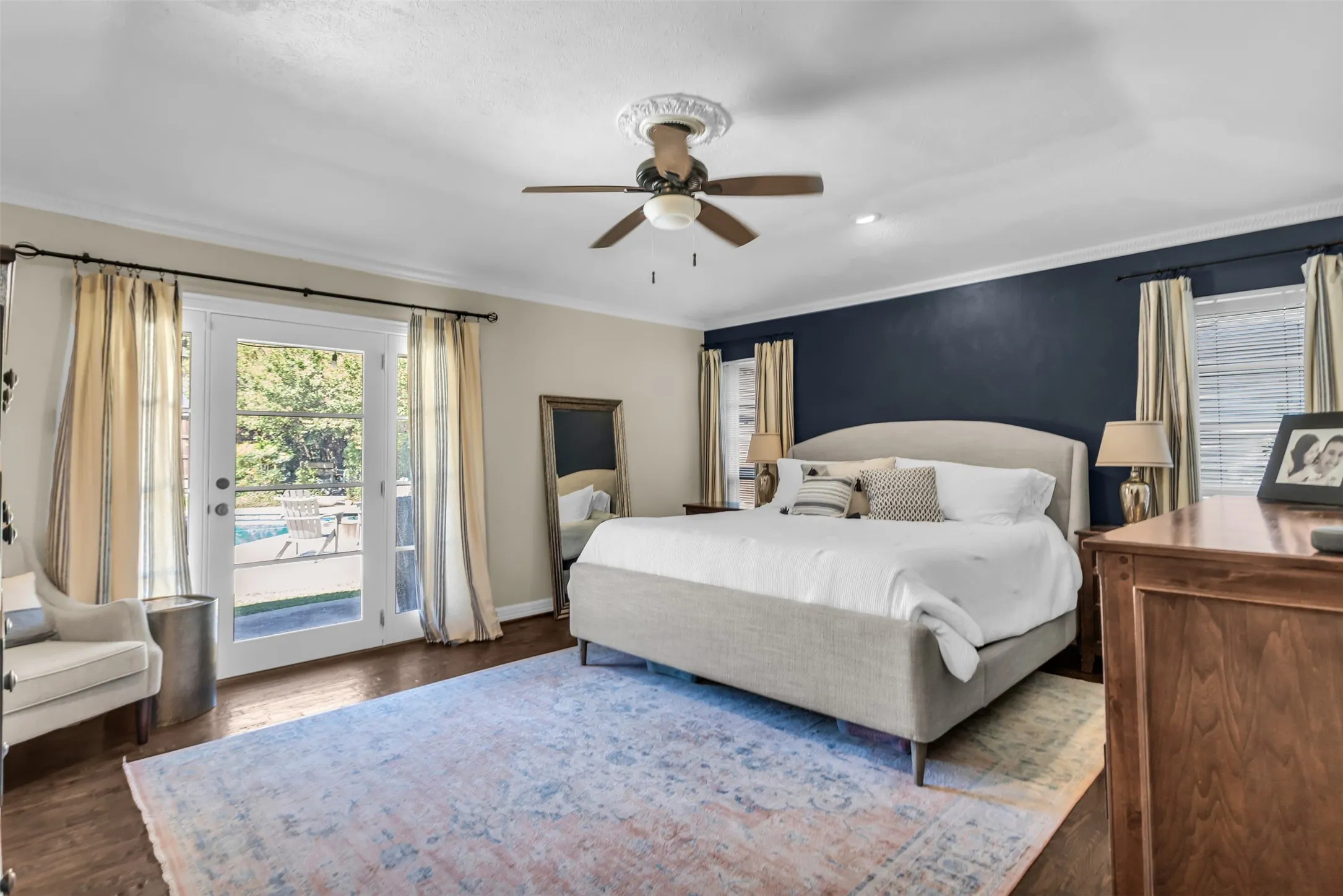 Hardwood-style flooring, crown molding, double French doors, ceiling fan, and accent wall