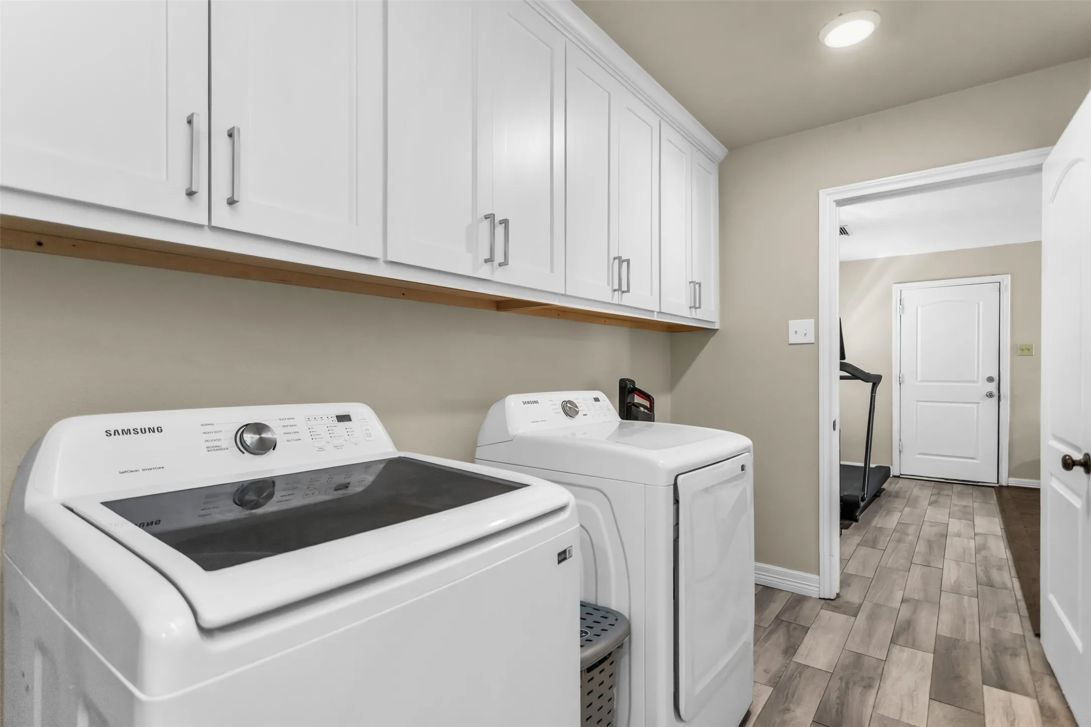 White shaker cabinetry with modern pulls, wood-finish flooring, and recessed ceiling lighting