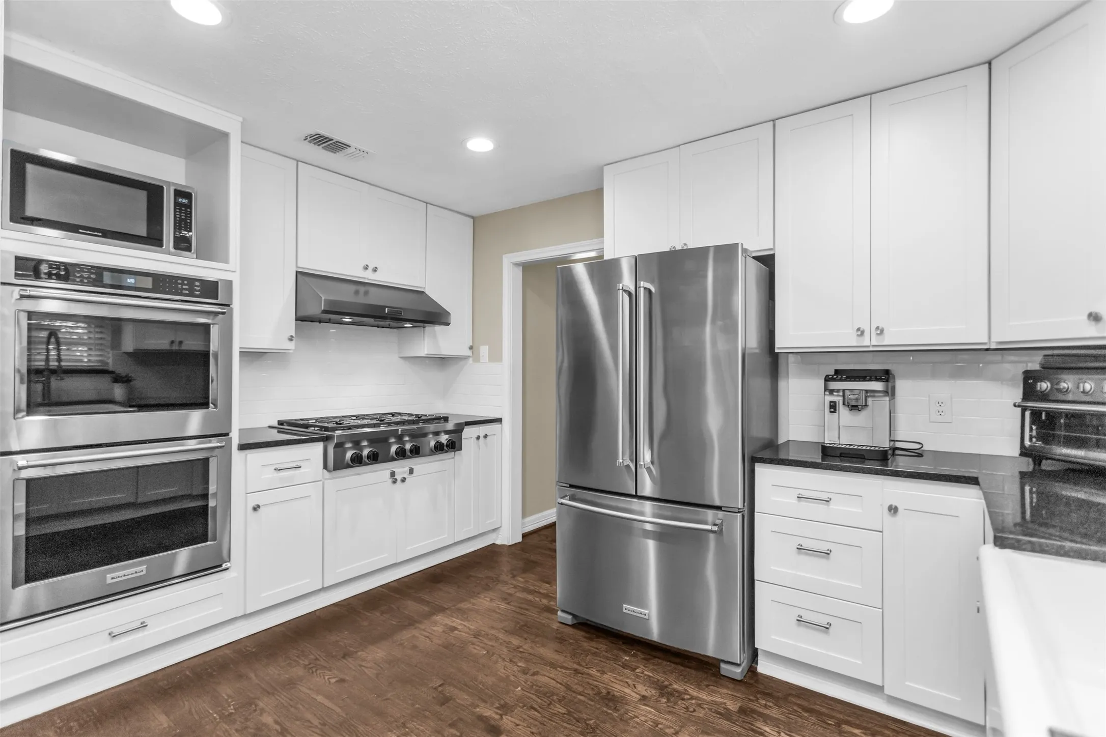 Kitchen featuring white cabinetry, dark countertops, wood-finish flooring, stainless steel appliances, and a tile backsplash