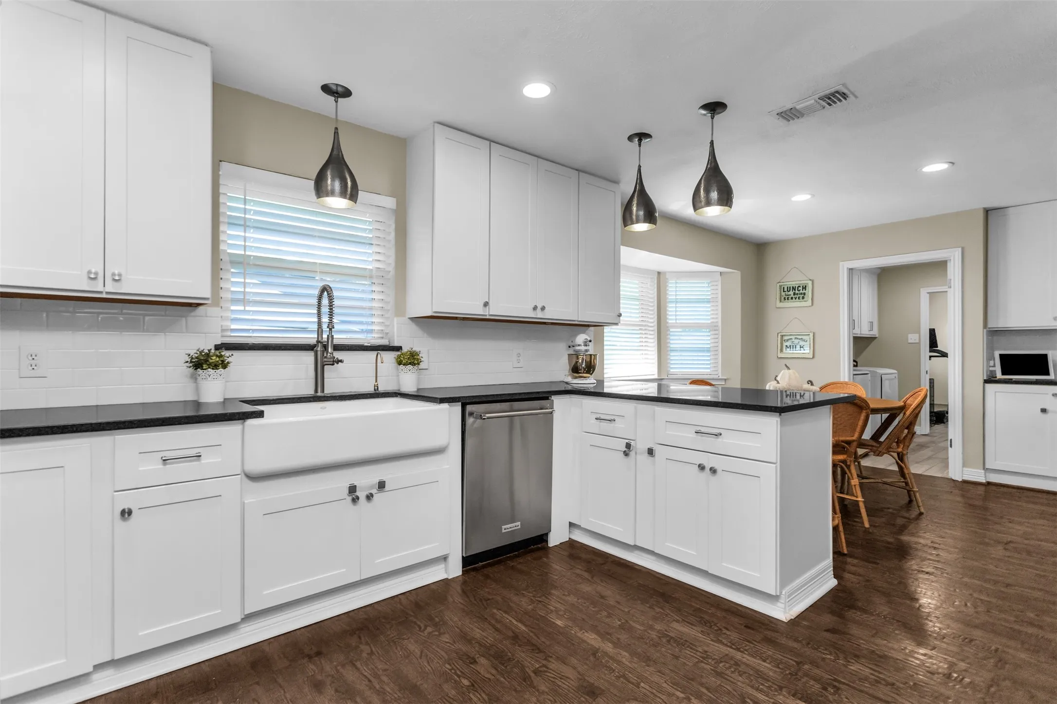 Contemporary kitchen featuring white shaker cabinetry, black quartz countertops, a farmhouse-style apron-front sink, and stainless steel appliances