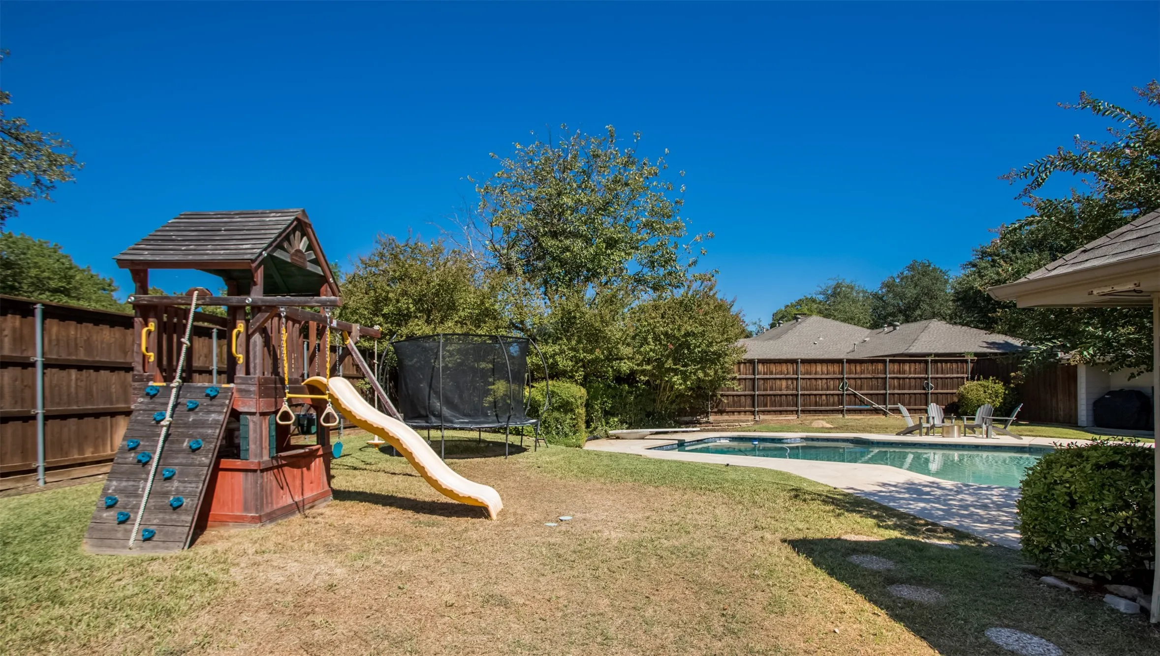 Expansive backyard featuring a built-in swimming pool with paved surround, wood privacy fencing, and mature trees
