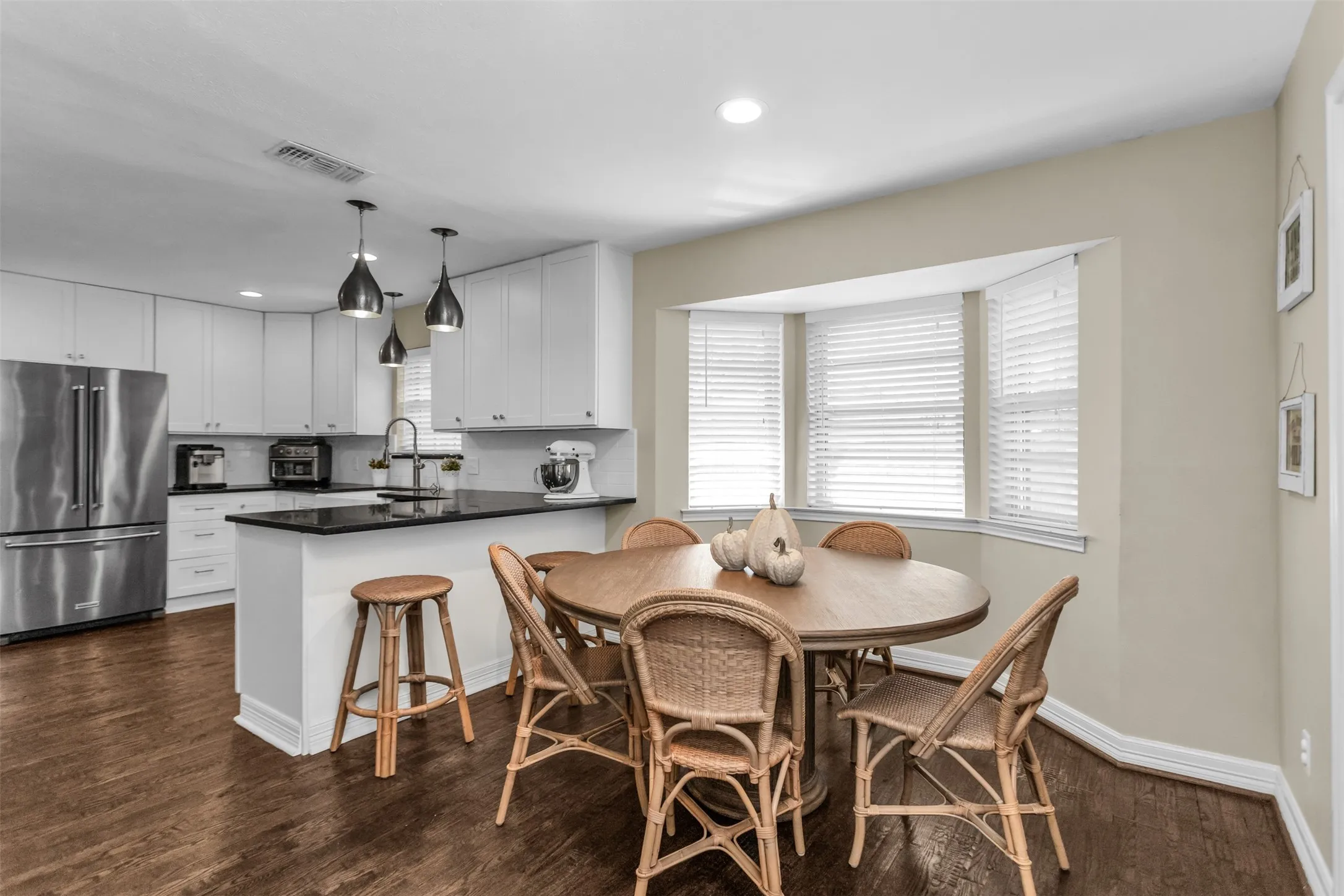 Kitchen featuring wood-finish flooring, white cabinetry, black countertops, stainless steel appliances, and a bay window