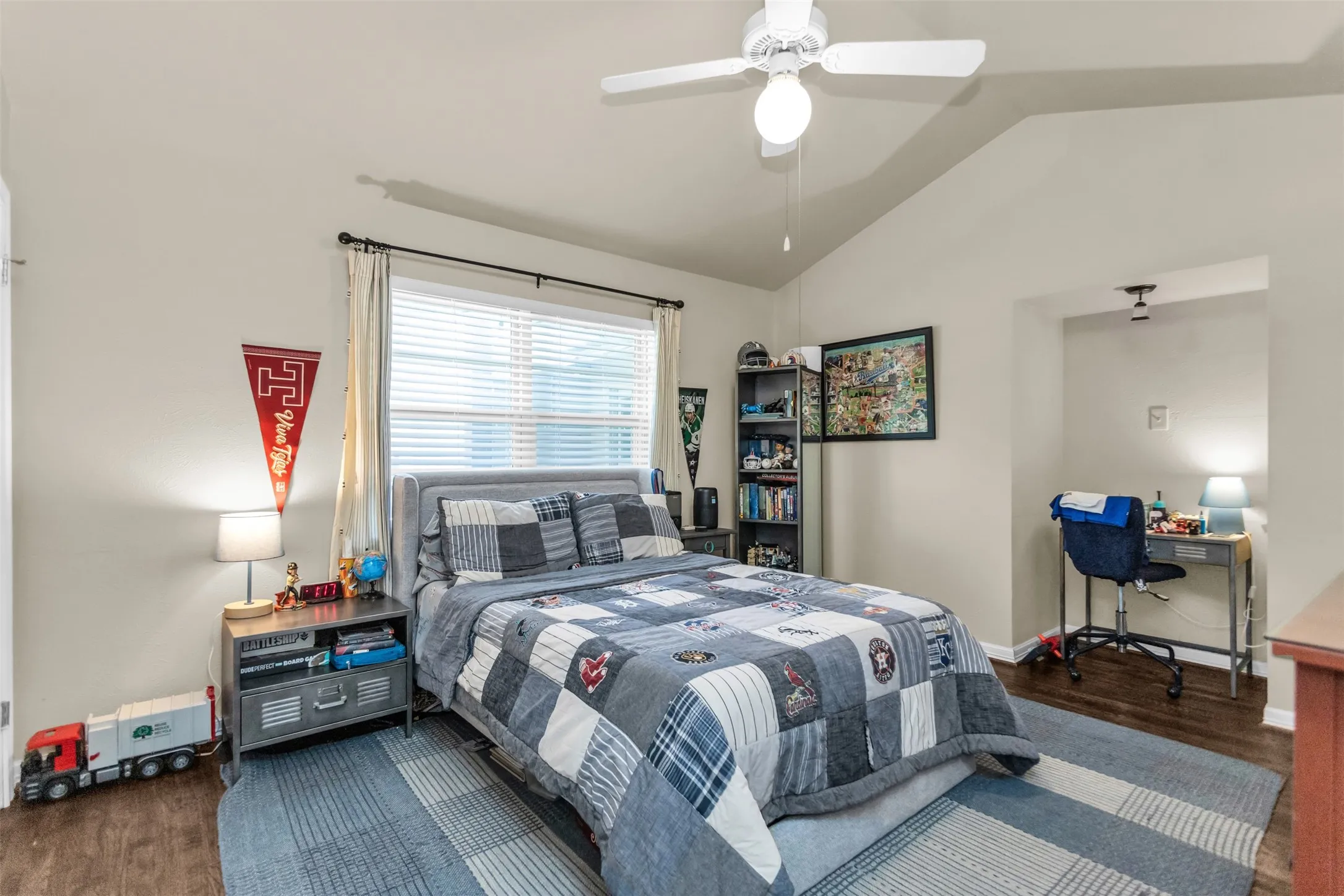 Spacious bedroom featuring vaulted ceilings, ceiling fan with integrated lighting, large windows with plantation shutters, wood-finish flooring, and a coordinating area rug
