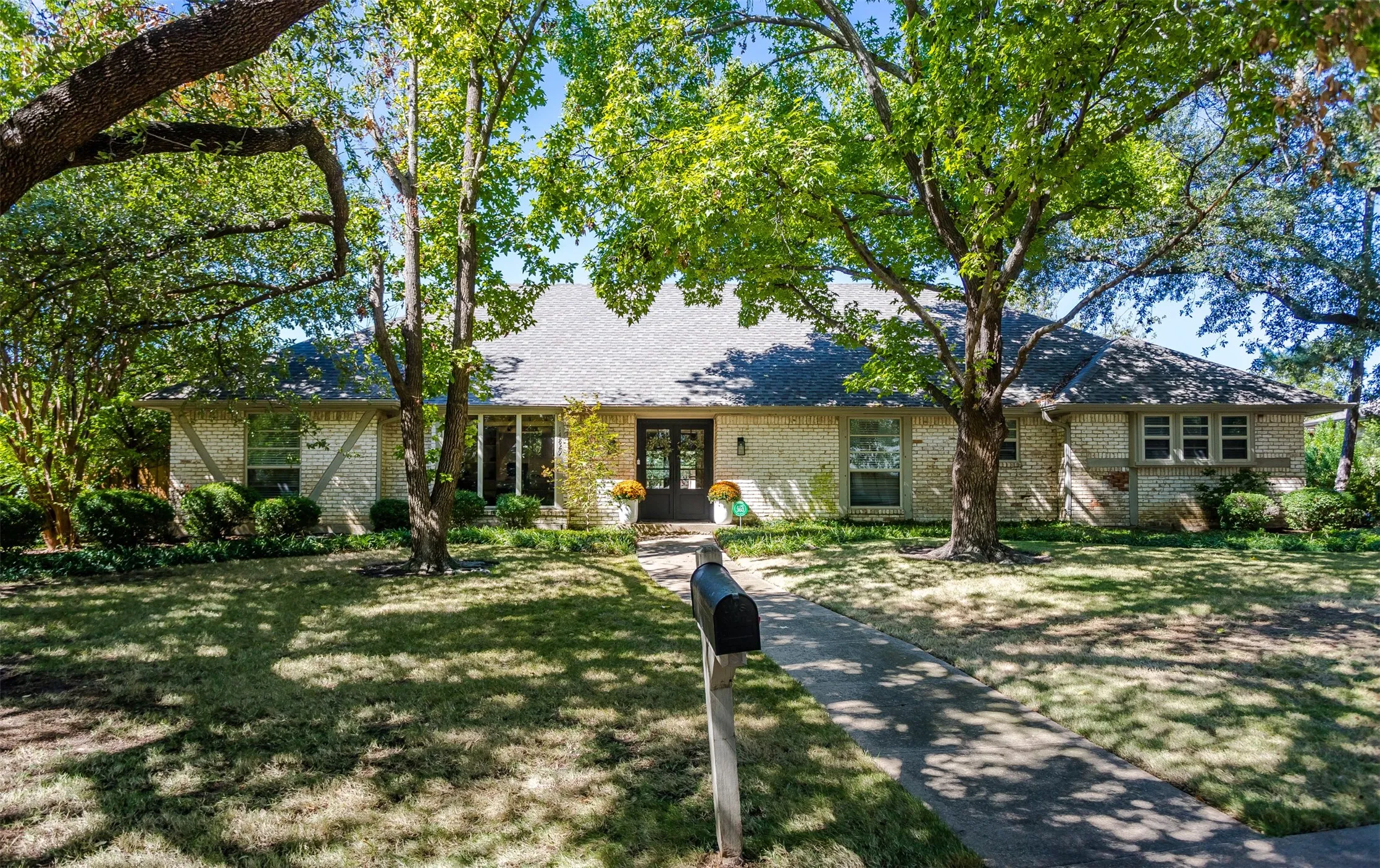 Charming single-story residence with a classic exterior featuring stone and stucco finishes, sheltered beneath mature oak trees