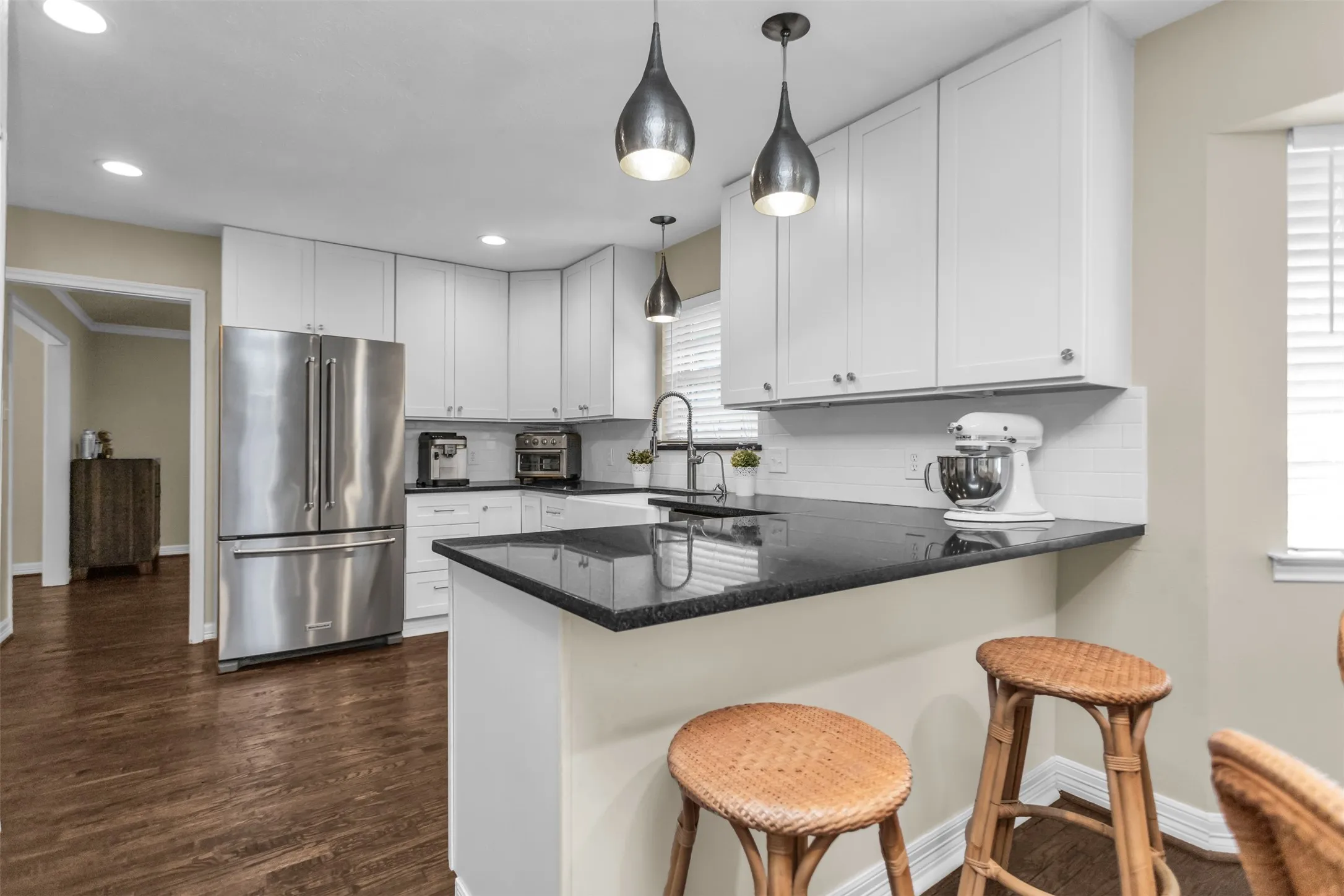 Modern kitchen featuring white cabinetry with black countertops, stainless steel French-door refrigerator, and pendant lighting with dark metal fixtures