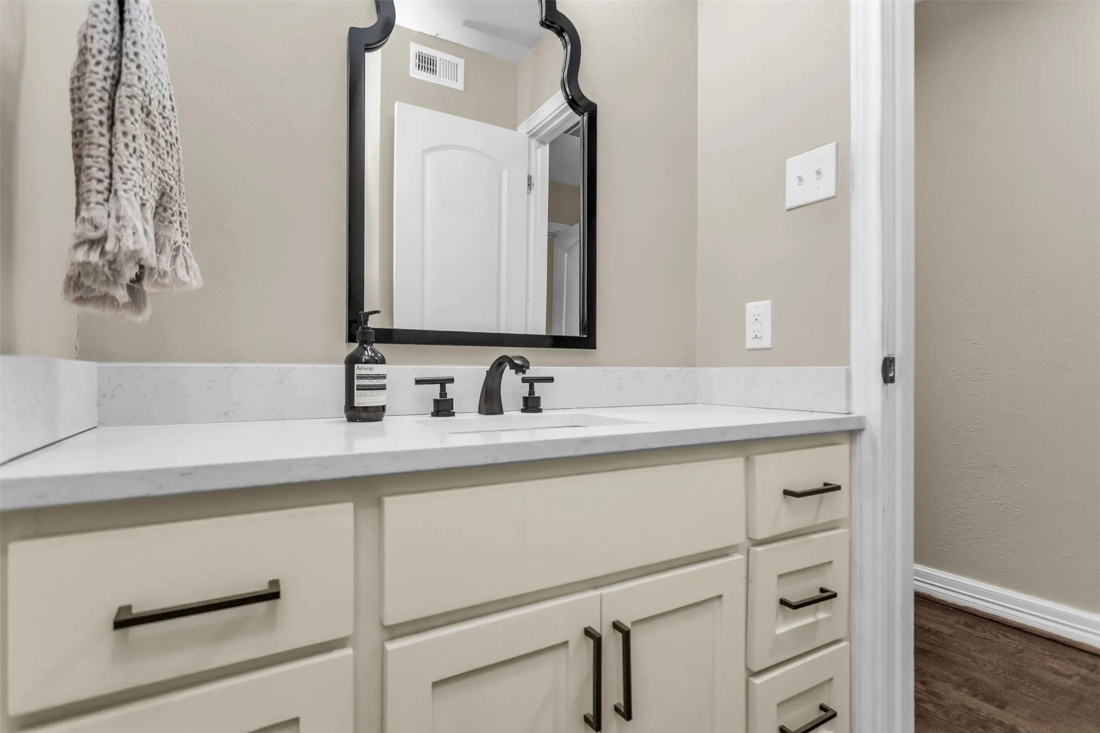 Bathroom vanity featuring a light-toned countertop with integrated sink, matte black faucet, and cream-colored cabinetry with dark hardware