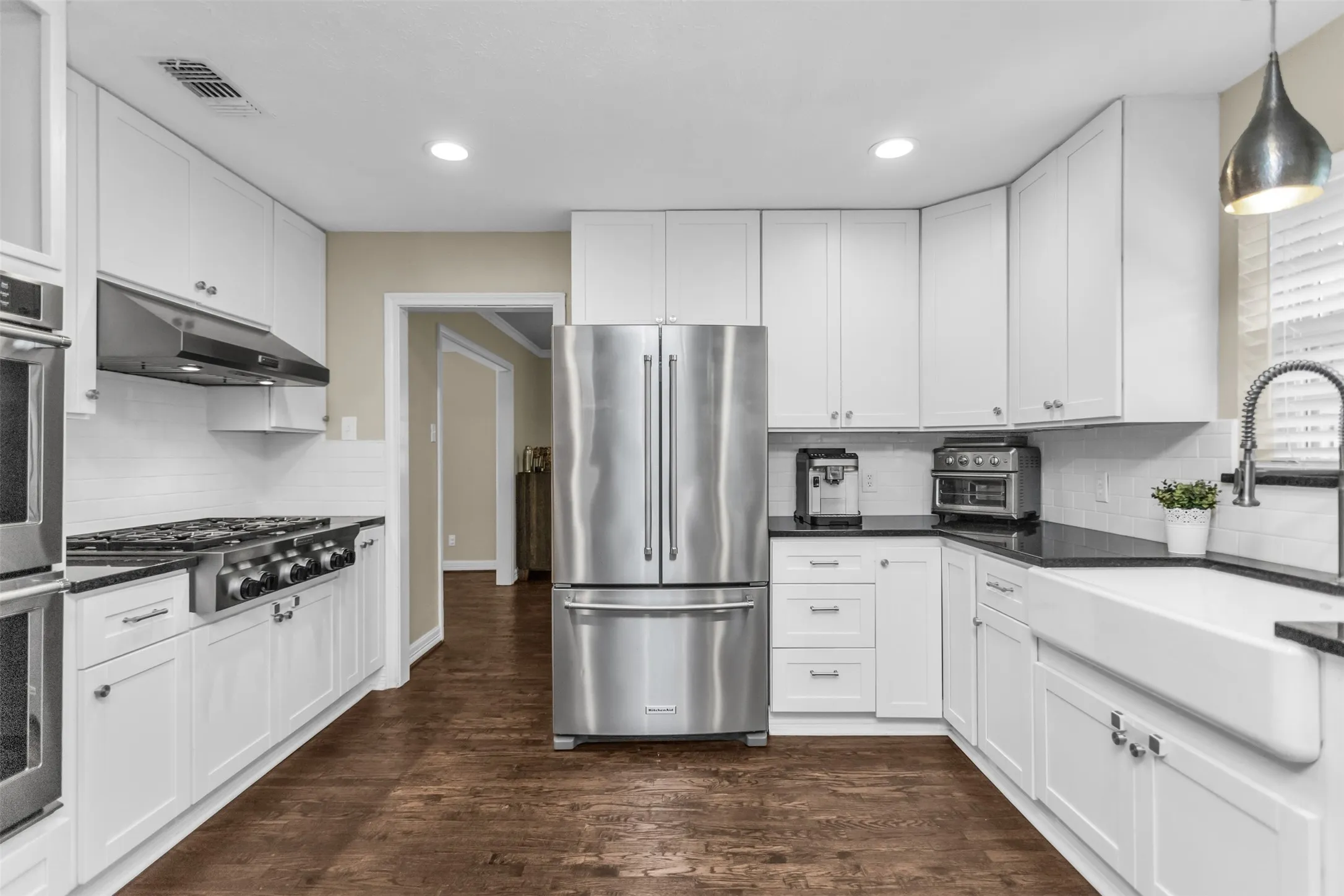 White shaker-style cabinetry, dark countertops, white subway tile backsplash, stainless steel appliances, and wood-finish flooring