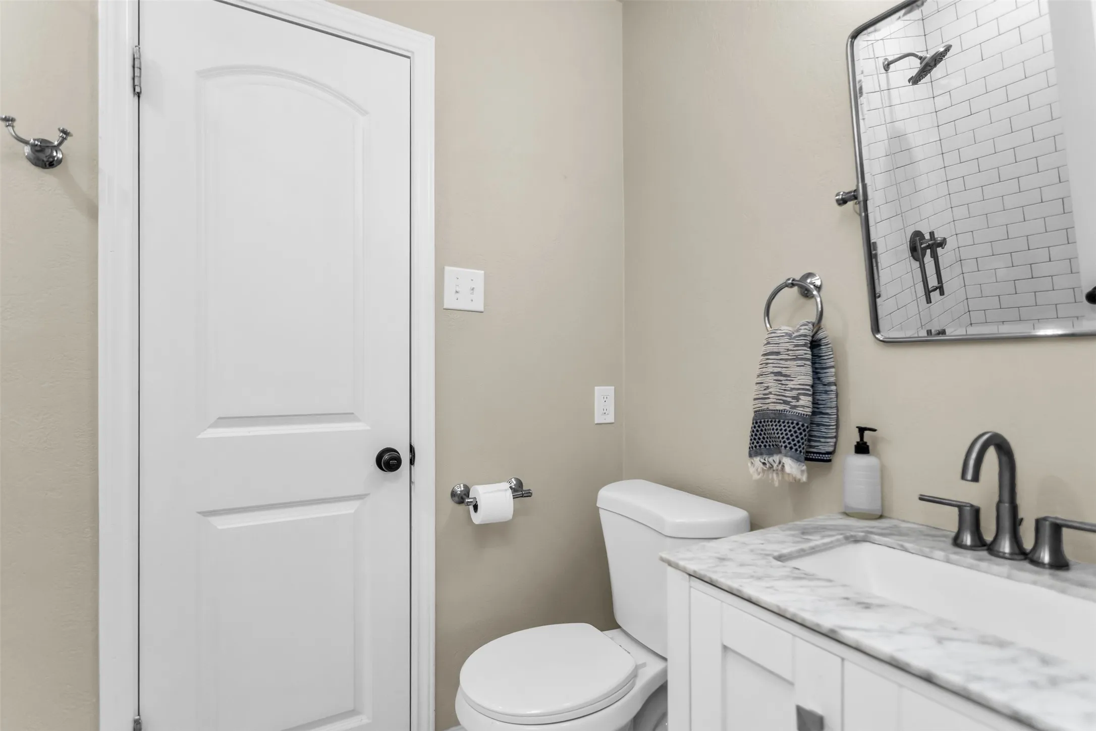 Modern bathroom featuring a white vanity with marble-look countertop, matte black faucet and hardware, white subway tile shower surround with frameless glass enclosure, white toilet, and soft neutral wall finishes​​‌​​​​‌​​‌‌​‌‌​​​‌‌​‌​‌​‌​​​‌​​ throughout