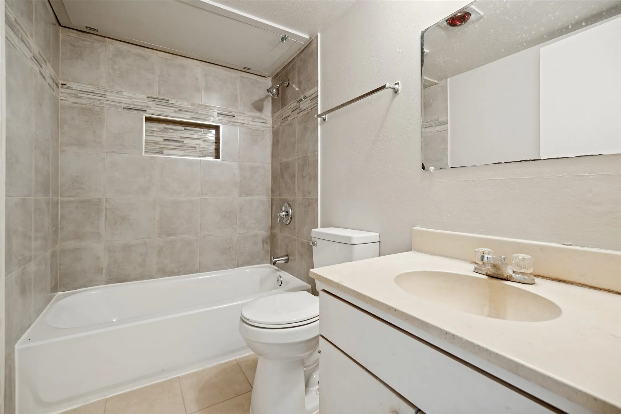 Recessed shower niche with mosaic tile accent, tiled shower walls, built-in bathtub, chrome shower fixture, and vanity with integrated sink