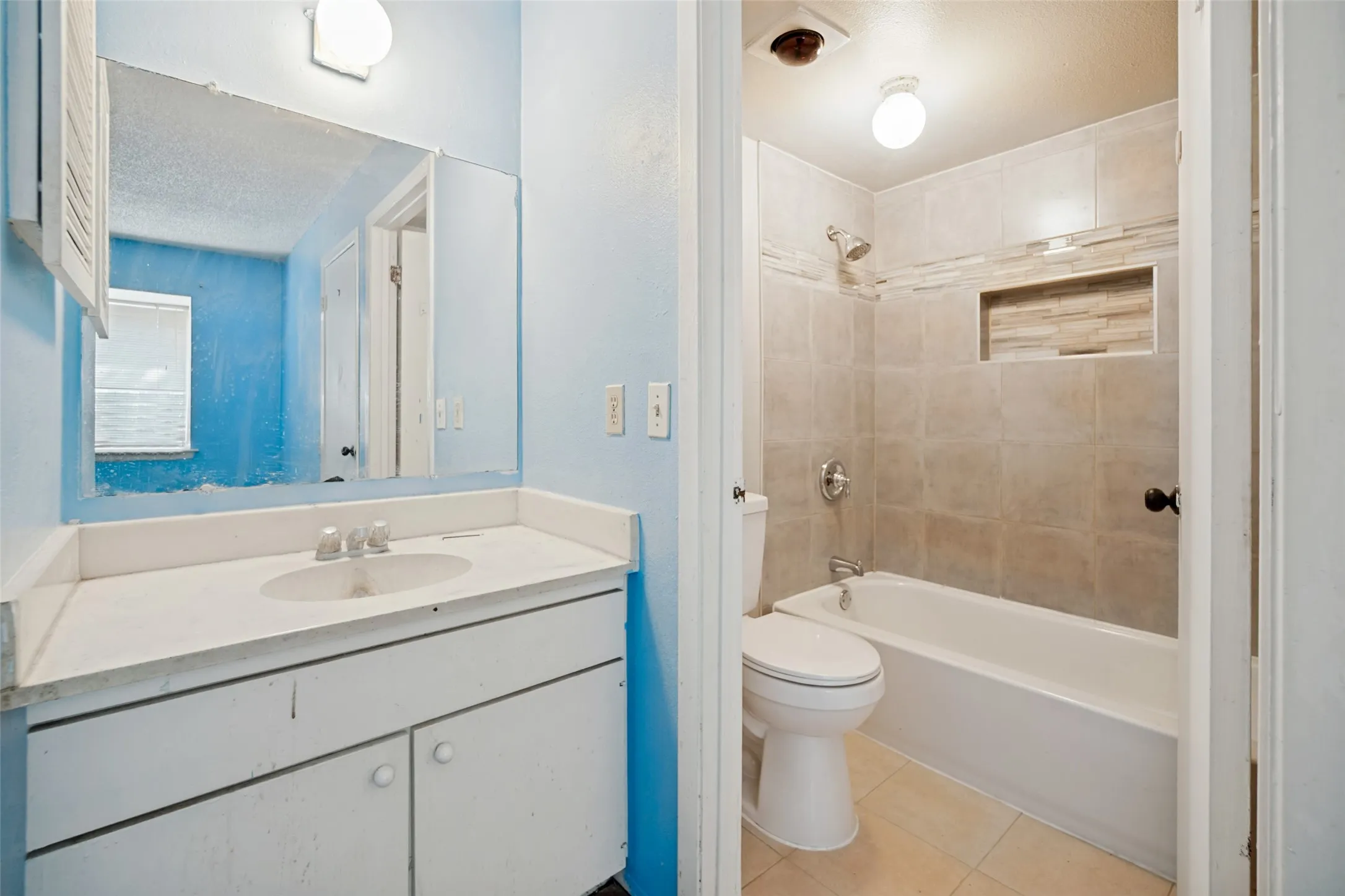 Bathroom featuring a vanity with an integrated sink, a large wall-mounted mirror, and a tub/shower combination with tiled walls and a recessed niche