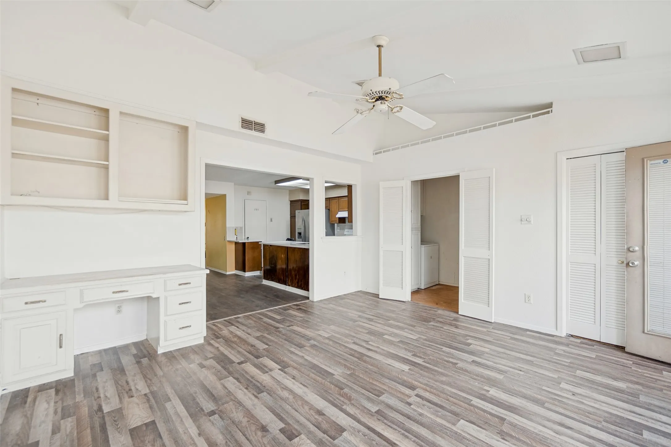 Wood-finish flooring, built-in desk with overhead shelving, vaulted ceiling, and ceiling fan
