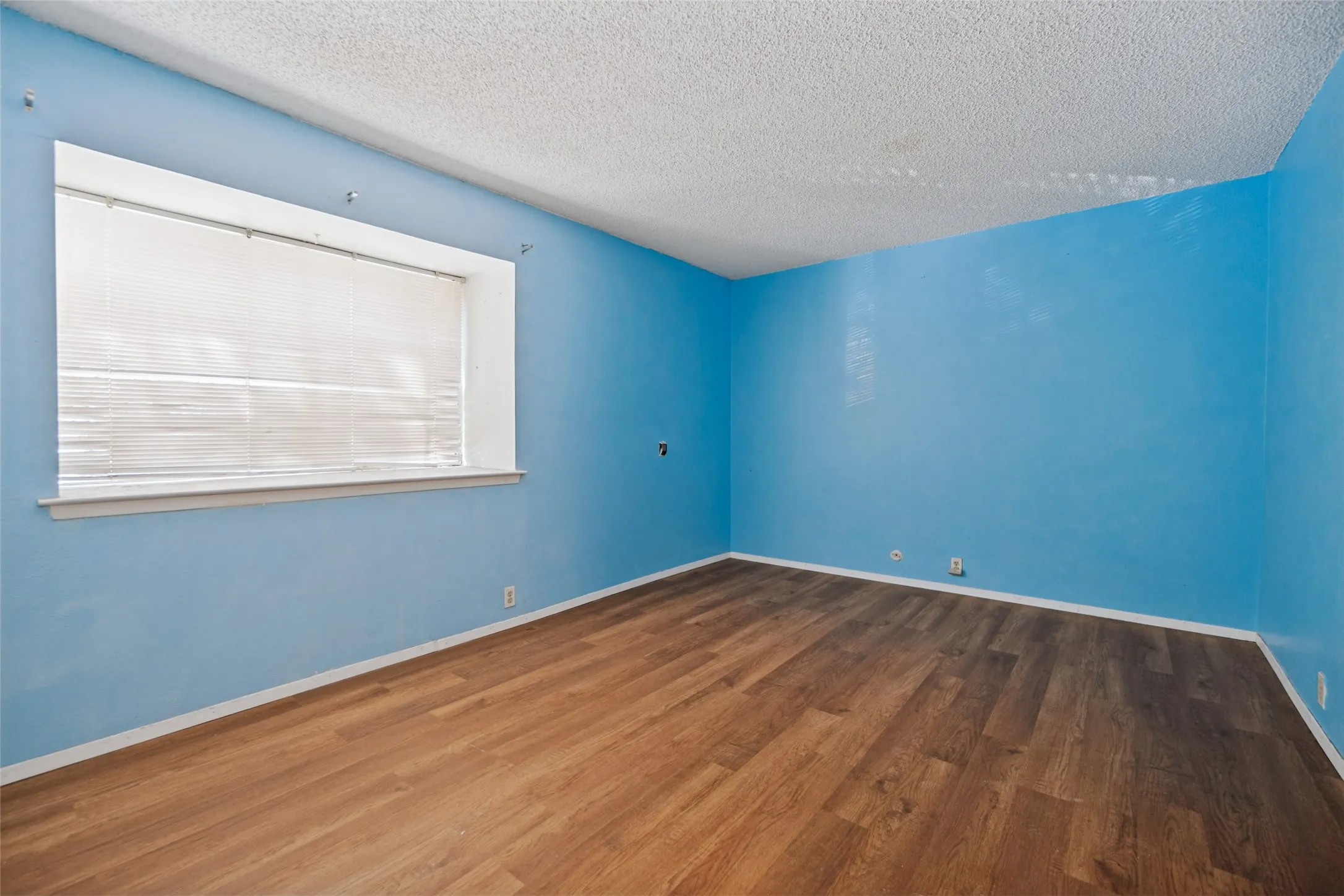 Wood-finish flooring with a window featuring white blinds