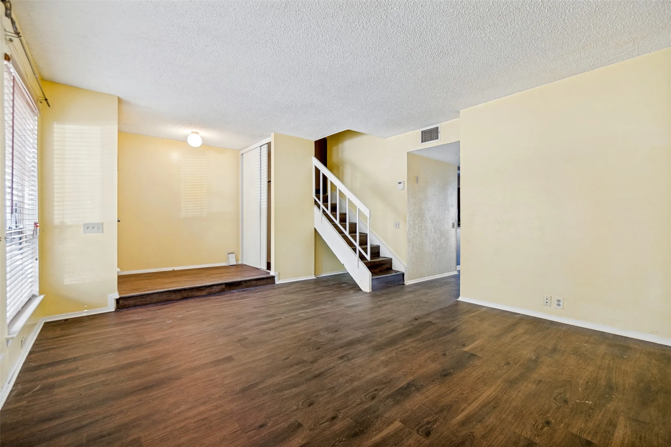 Wood-finish flooring, staircase with white railing, built-in storage closet, and ceiling-mounted light fixture