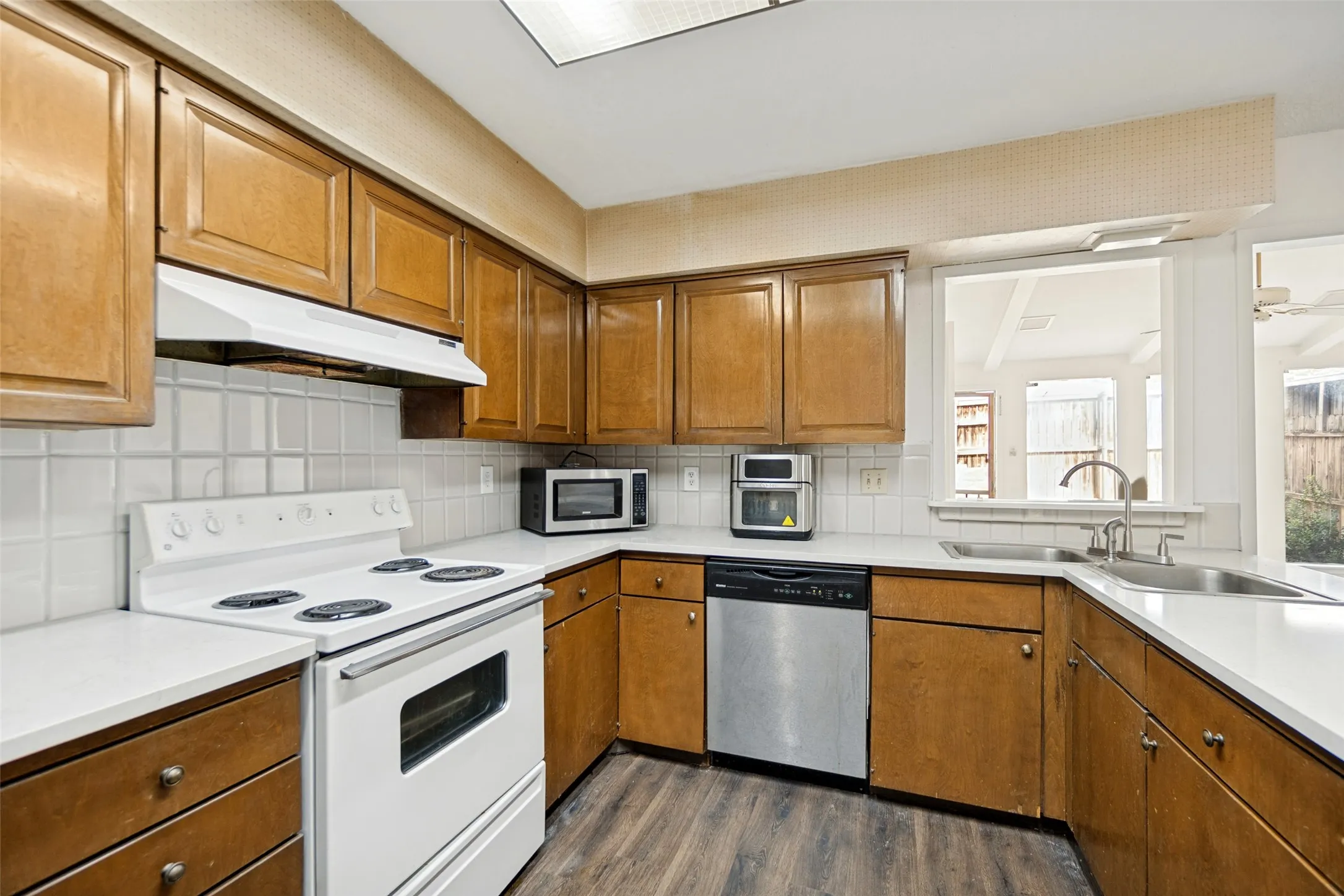 Wood-finish flooring, wood cabinetry, white tile backsplash, white countertops, and a double basin stainless steel sink